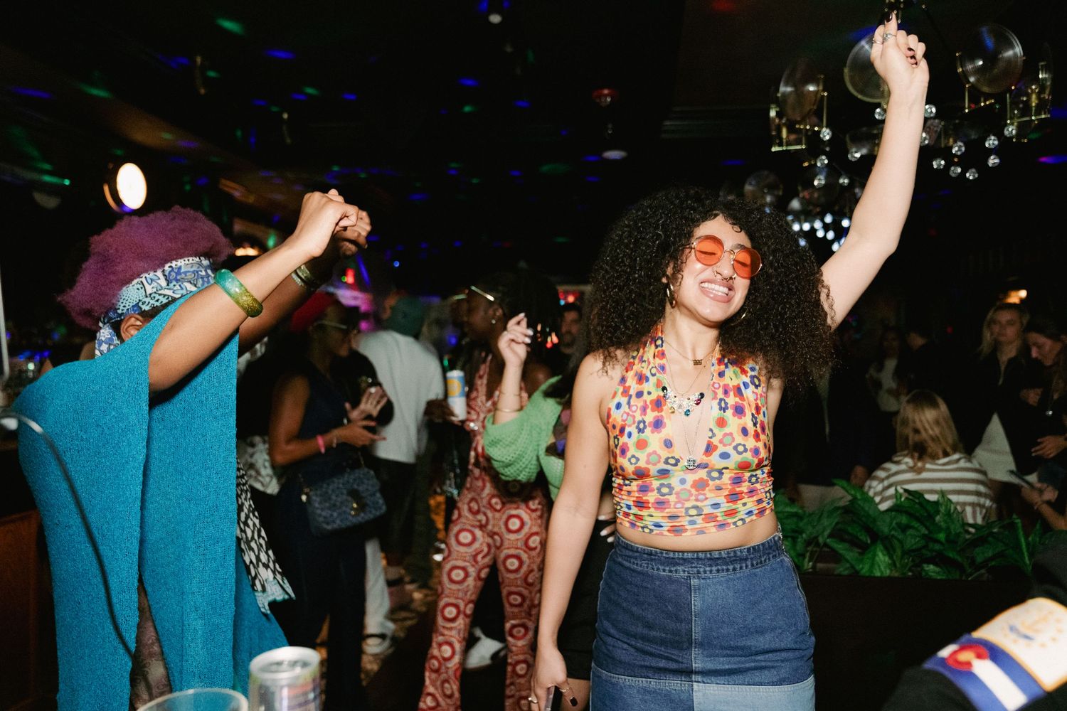People dancing and celebrating at a lively nighttime party with colorful lighting and foliage in the background. Boston MA photographer.