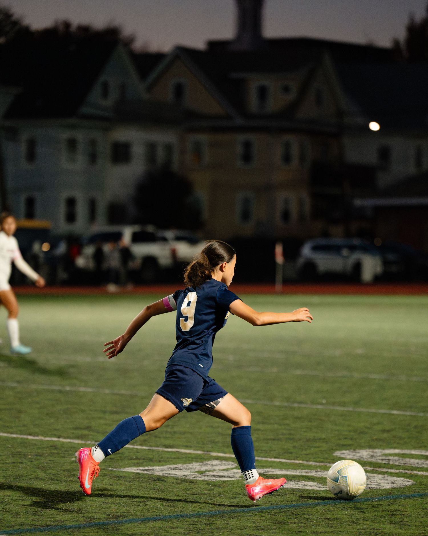 Soccer player in navy blue uniform slides to kick ball on illuminated field at night. Boston MA photographer, Malden MA and Greater Boston.