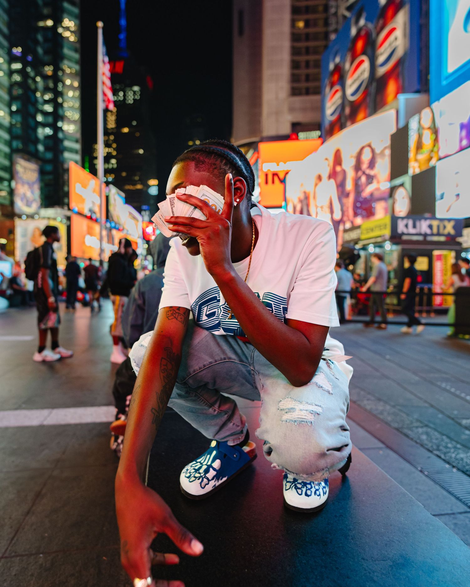 Person in white t-shirt crouching on illuminated city street at night surrounded by bright neon signs and billboards. Boston MA photographer