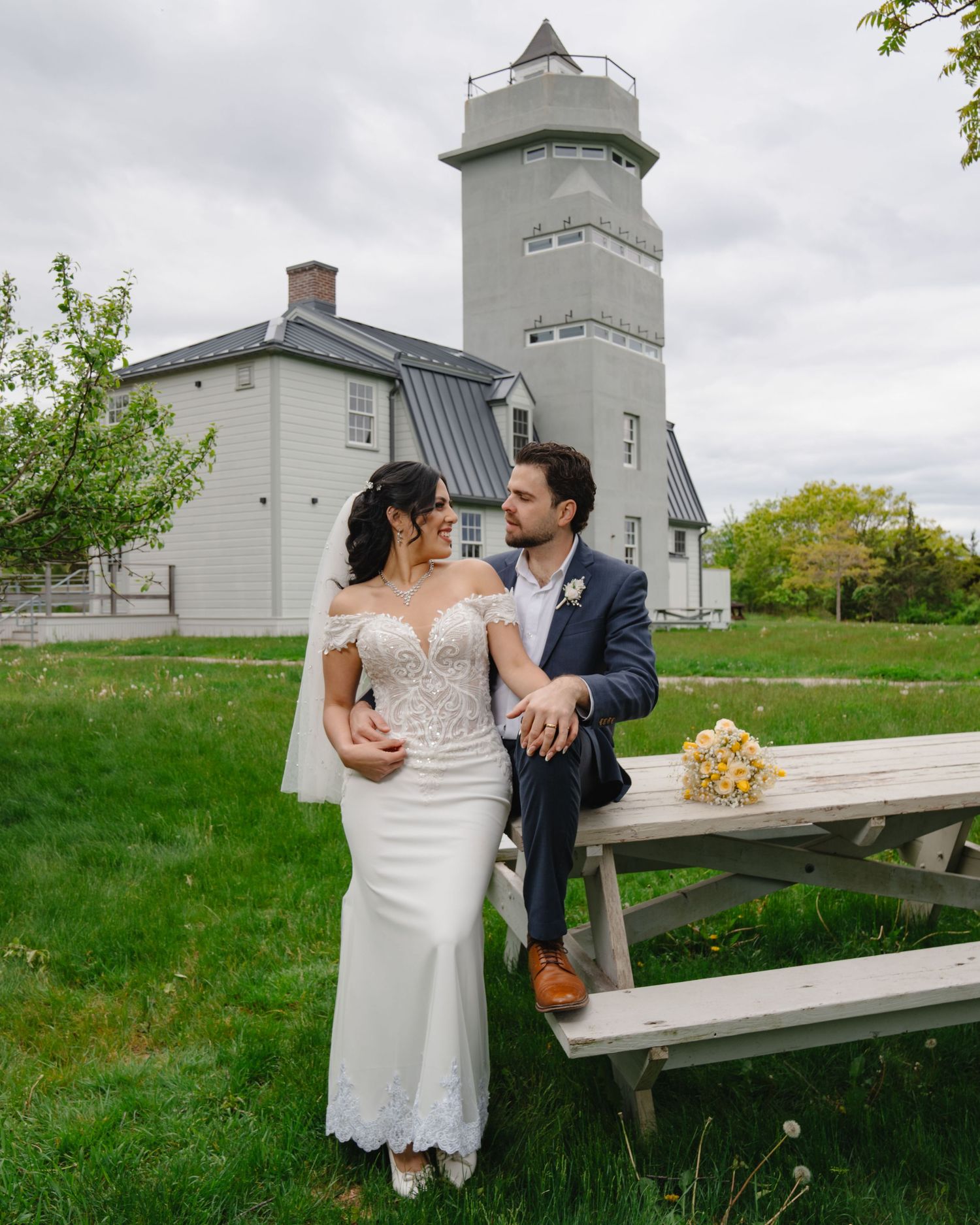 A couple shares romantic moments on a bench near a white lighthouse on a cloudy day. Boston MA photographer, Malden MA & Greater Boston Area