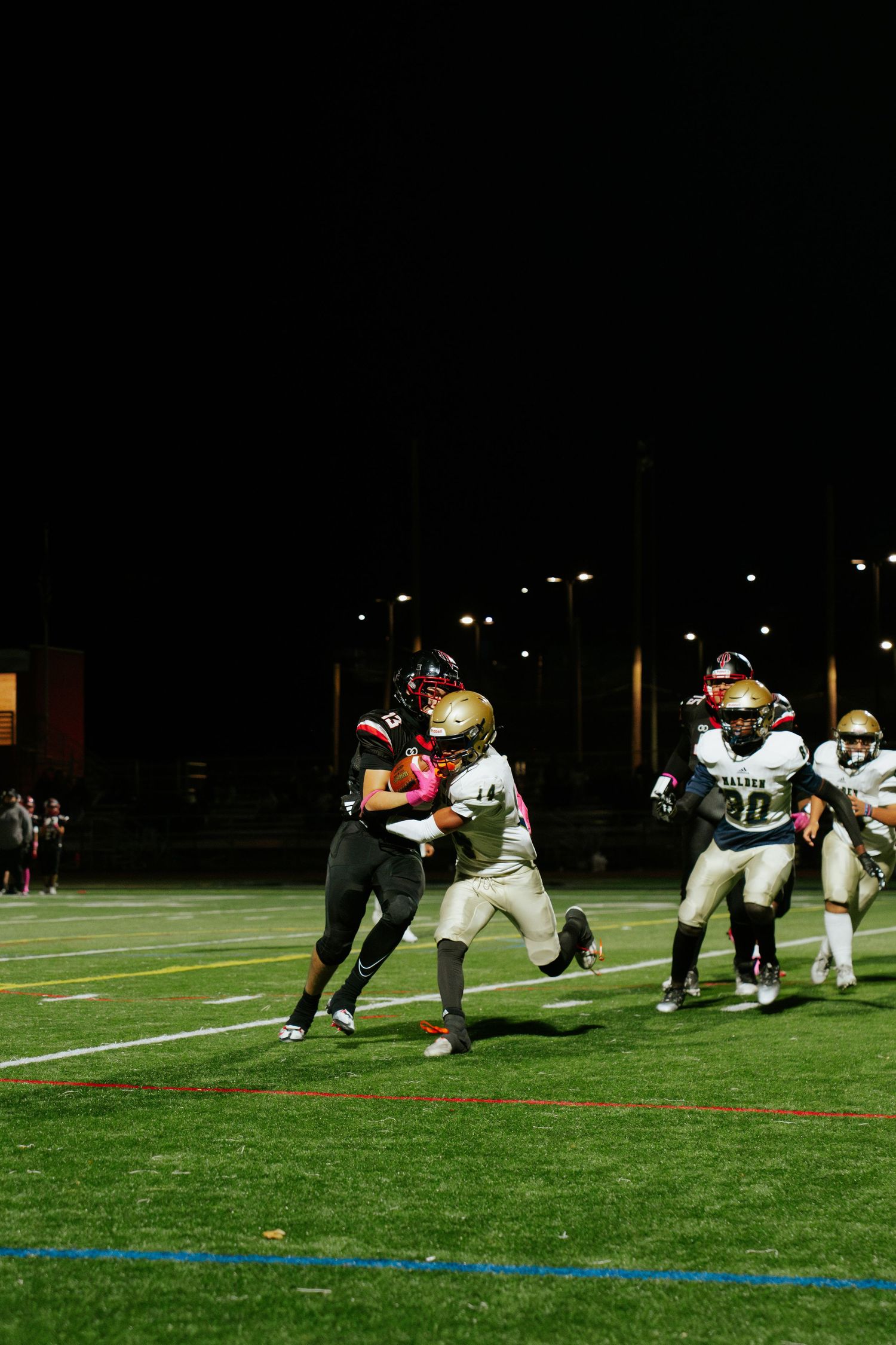 Football players line up at the line of scrimmage during a nighttime game on an illuminated field. Boston MA photographer, Malden MA.
