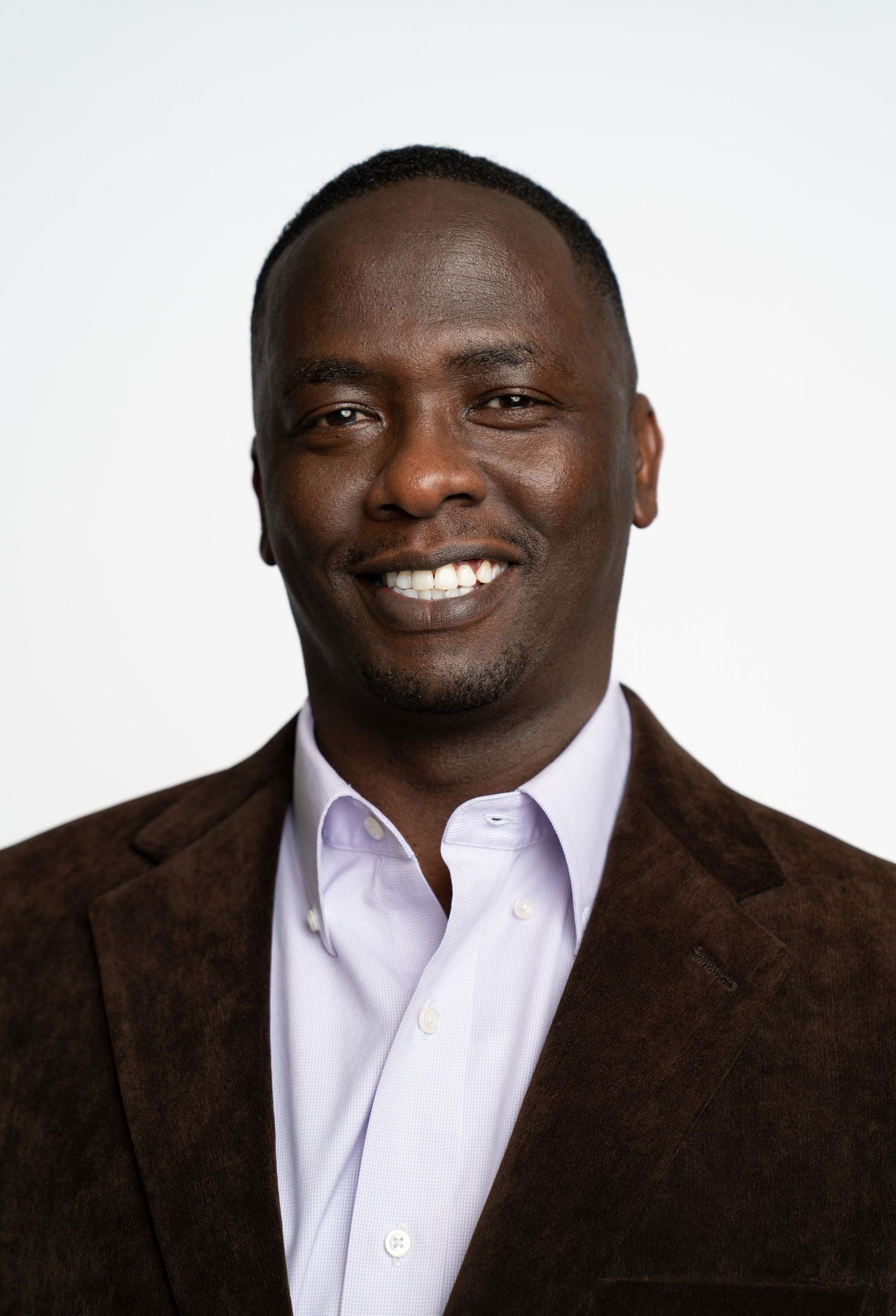 Portrait of someone in a brown suit jacket and white shirt against a white background, smiling warmly. Boston MA photographer, Malden MA.