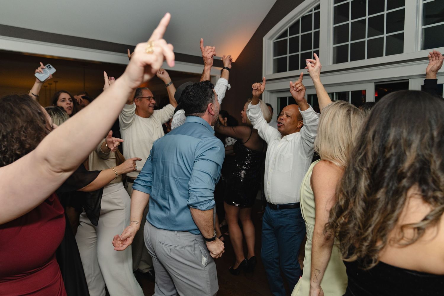 A lively crowd of party guests dancing with raised hands and drinks at an indoor celebration event. Greater Boston Area photographer, Malden