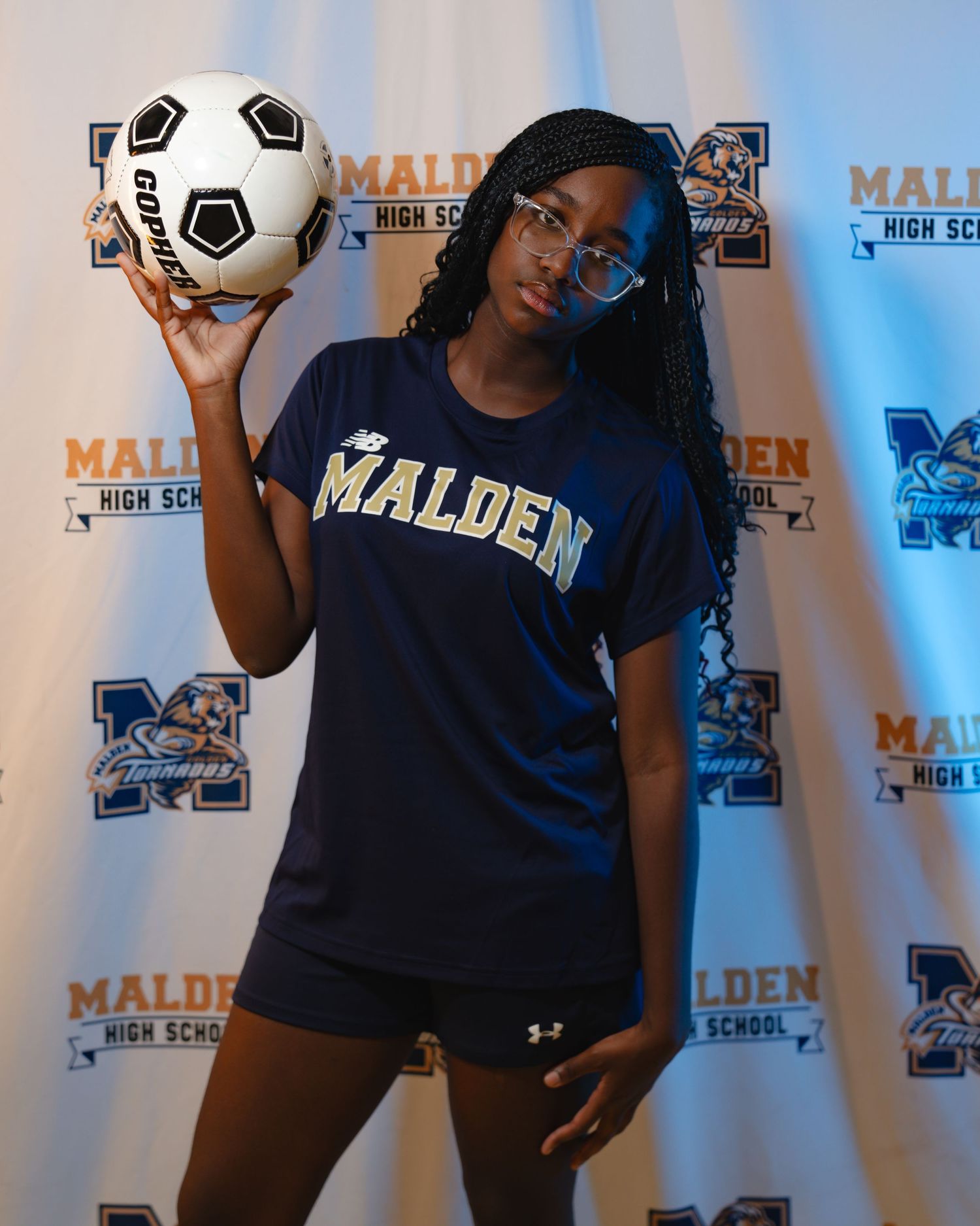 Person in navy blue Malden sports apparel poses with soccer ball against branded backdrop in multiple shots. Boston MA photographer. Media