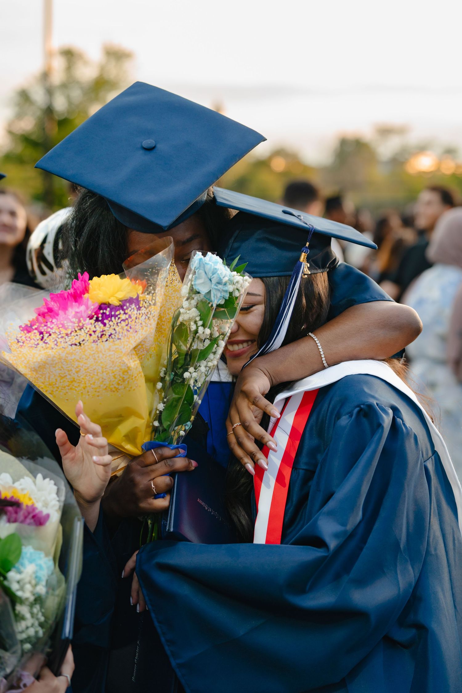 Graduates in blue caps and gowns holding colorful flower bouquets during commencement ceremony celebration. Boston MA photographer, Malden.