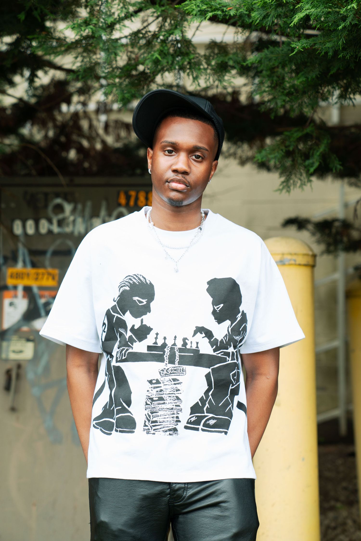 Person wearing a black cap and white graphic t-shirt with silhouette design stands against outdoor background. Boston MA photographer.