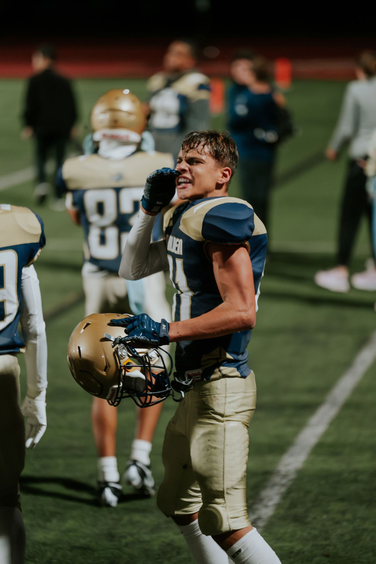 Football player in gold and navy uniform holding helmet on field during game or practice session. Boston MA photographer, Malden MA.