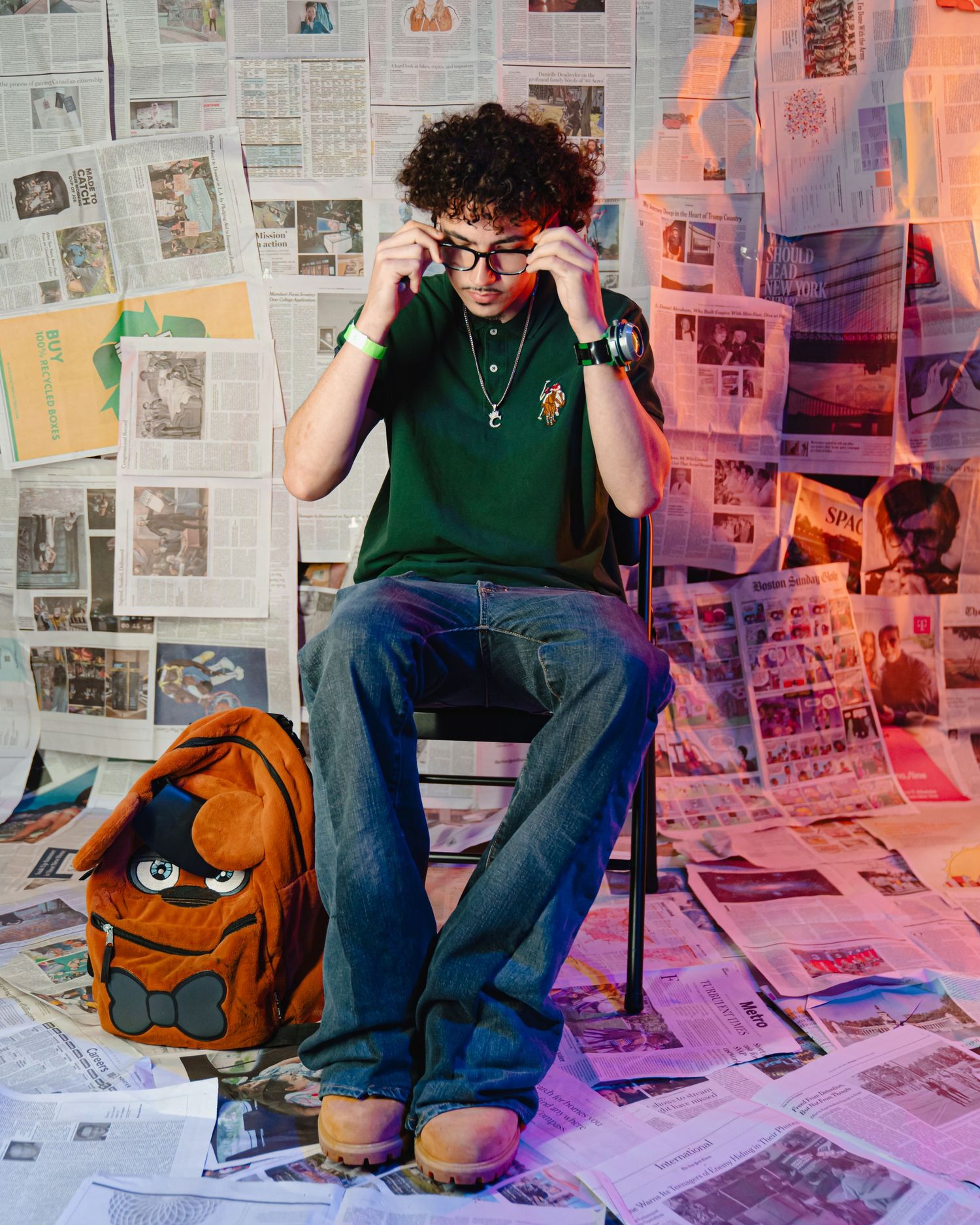 Person in green shirt sits among colorful newspaper pages and Freddy back pack creating an artistic scene. Boston MA photographer.