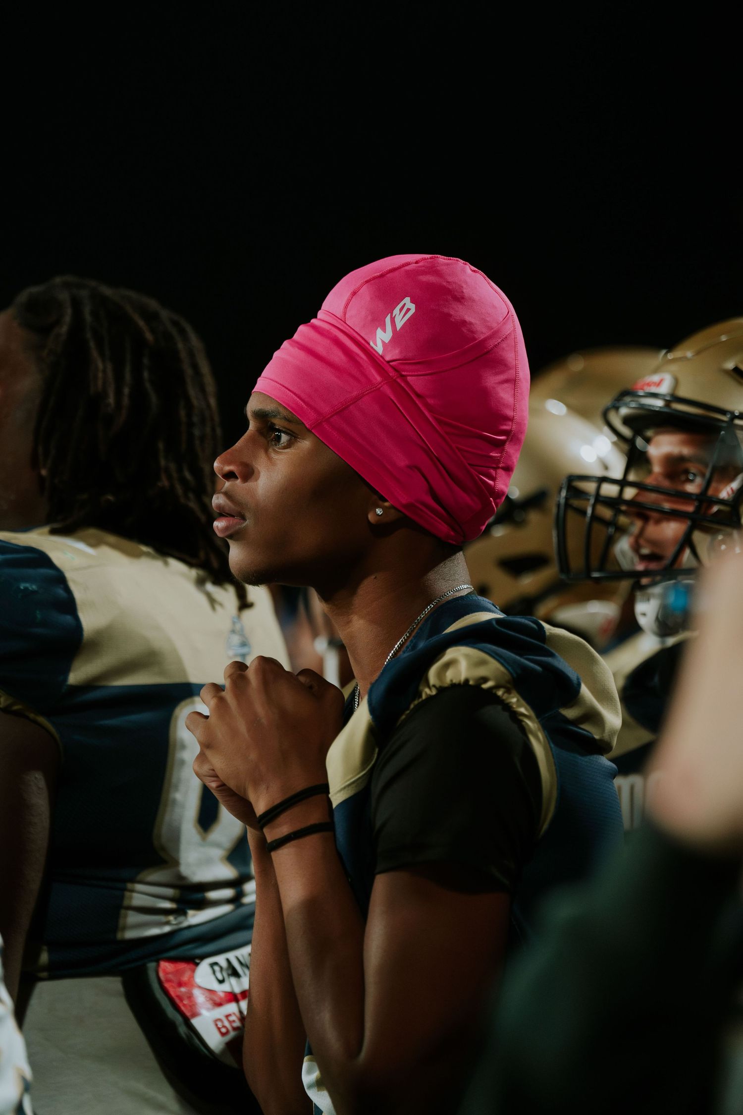 Person wearing a bright pink beanie sits in contemplation during what appears to be an indoor gathering. Boston MA photographer, Malden MA.