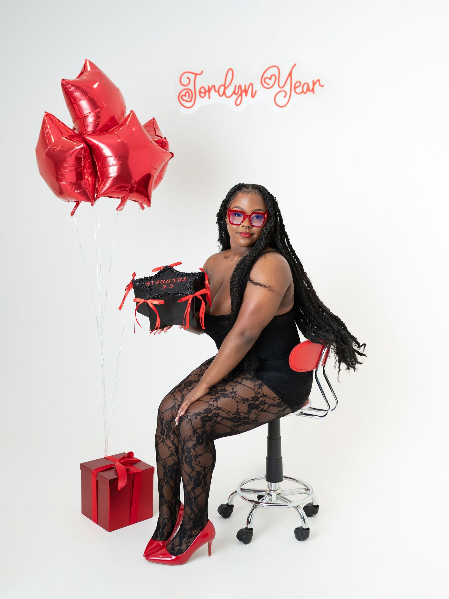 A stylish figure in red heels and lace poses with red gift boxes and bows against a white backdrop. Boston MA photographer, Malden MA.
