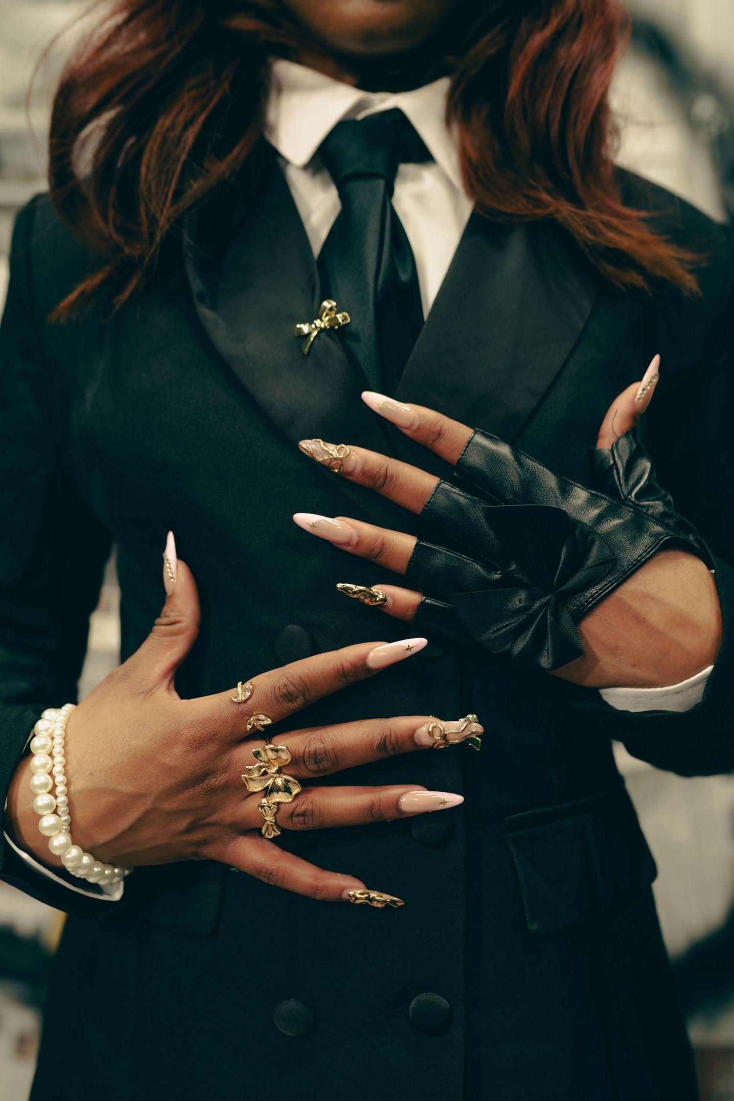 Close-up of hands wearing black leather gloves, pearl bracelet and gold rings against a dark formal suit with tie. Boston MA photographer.