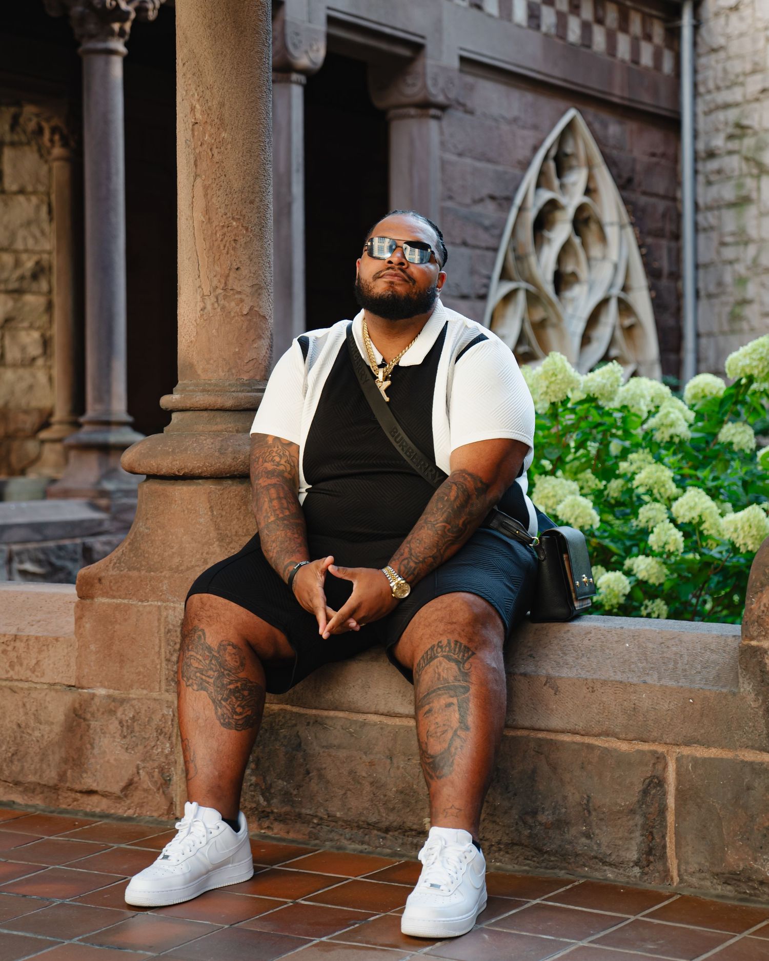 Someone wearing white sneakers and shorts sitting on stone steps near green hydrangea bushes. Boston MA photographer, Malden MA.