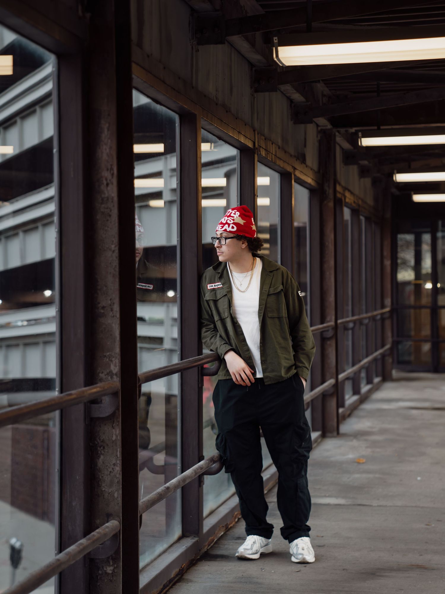 Person wearing olive bomber jacket and black pants stands in concrete hallway with modern architectural details. Boston MA photographer.