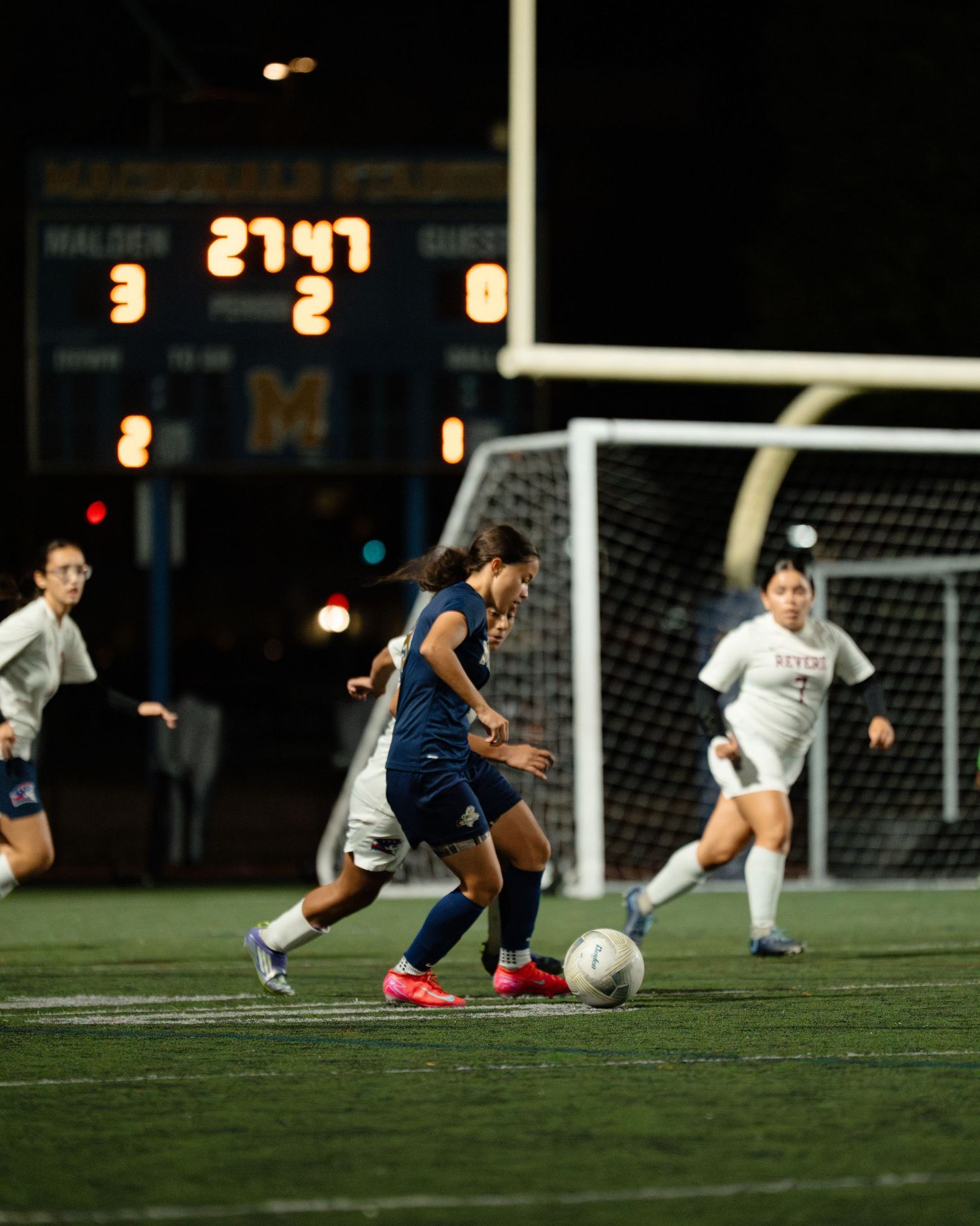 Soccer players battle for possession of the ball during an intense nighttime match under stadium lights. Boston MA photographer, Malden MA.
