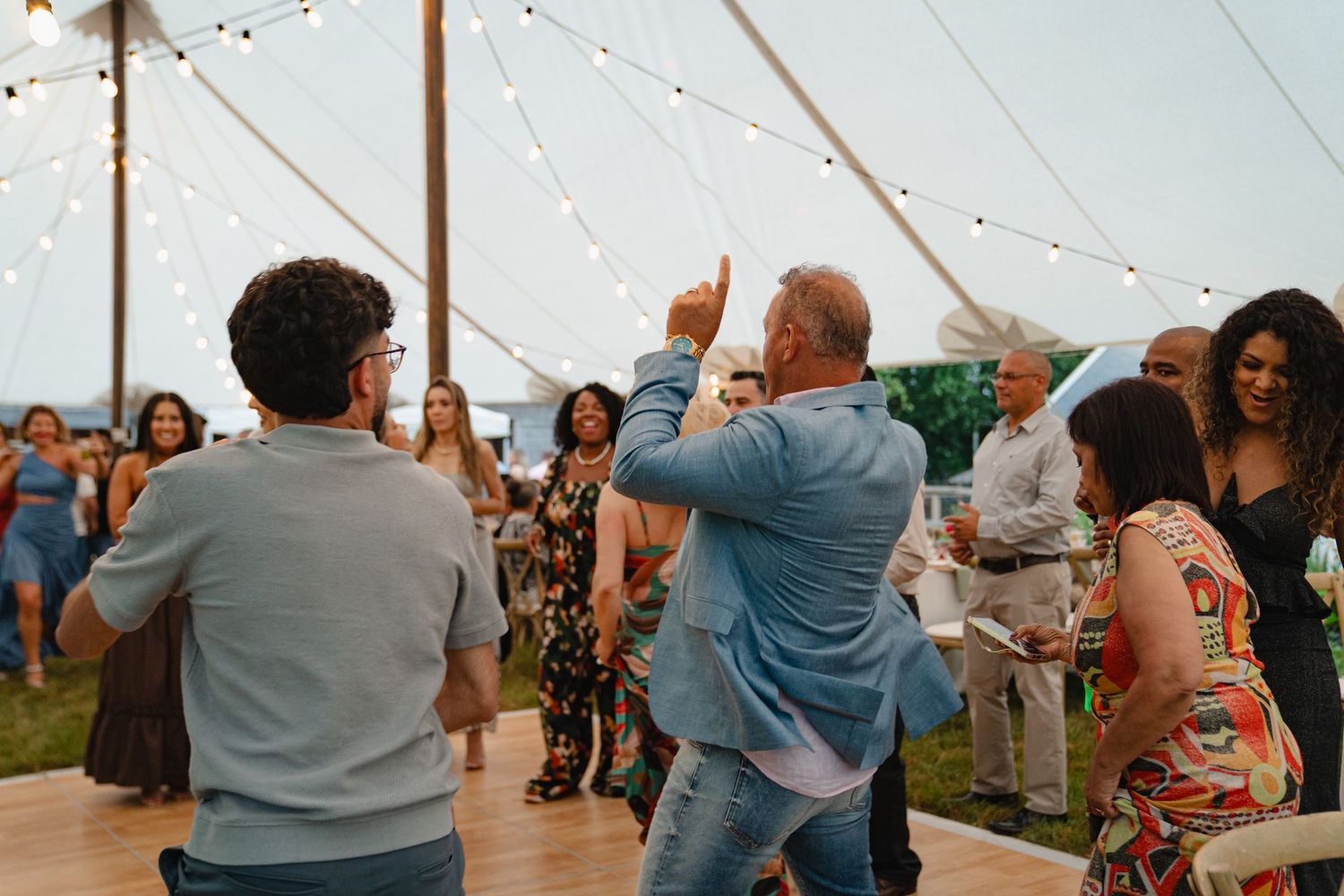 People dancing and celebrating together inside a large white tent during a birthday party. Boston MA photographer, Malden MA.