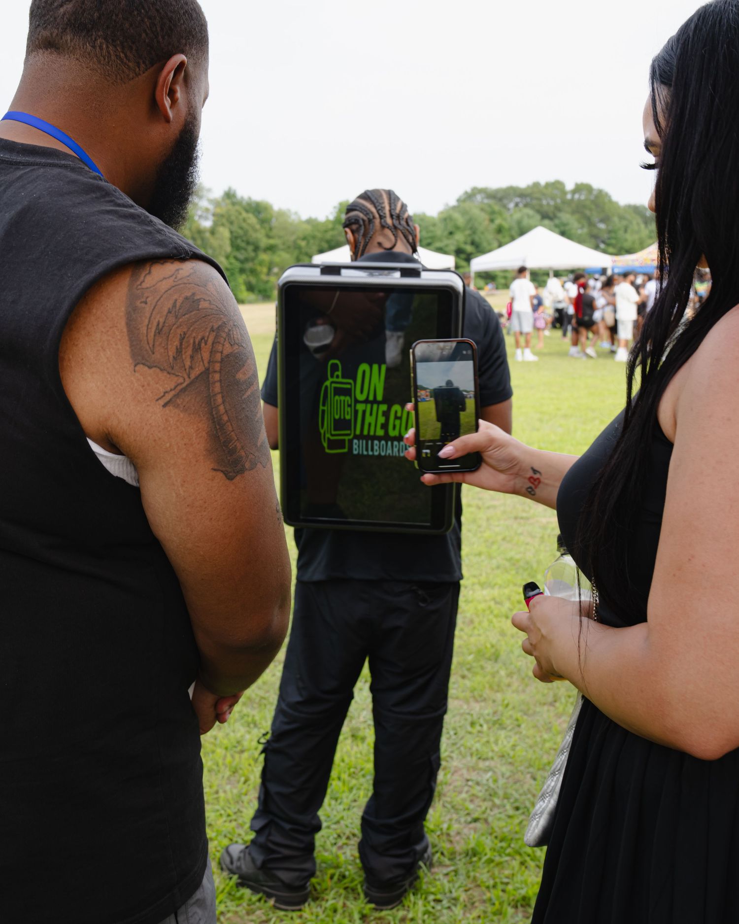 People looking at a digital display showing green text at an outdoor event with tents in the background. Boston MA photographer, Malden MA.
