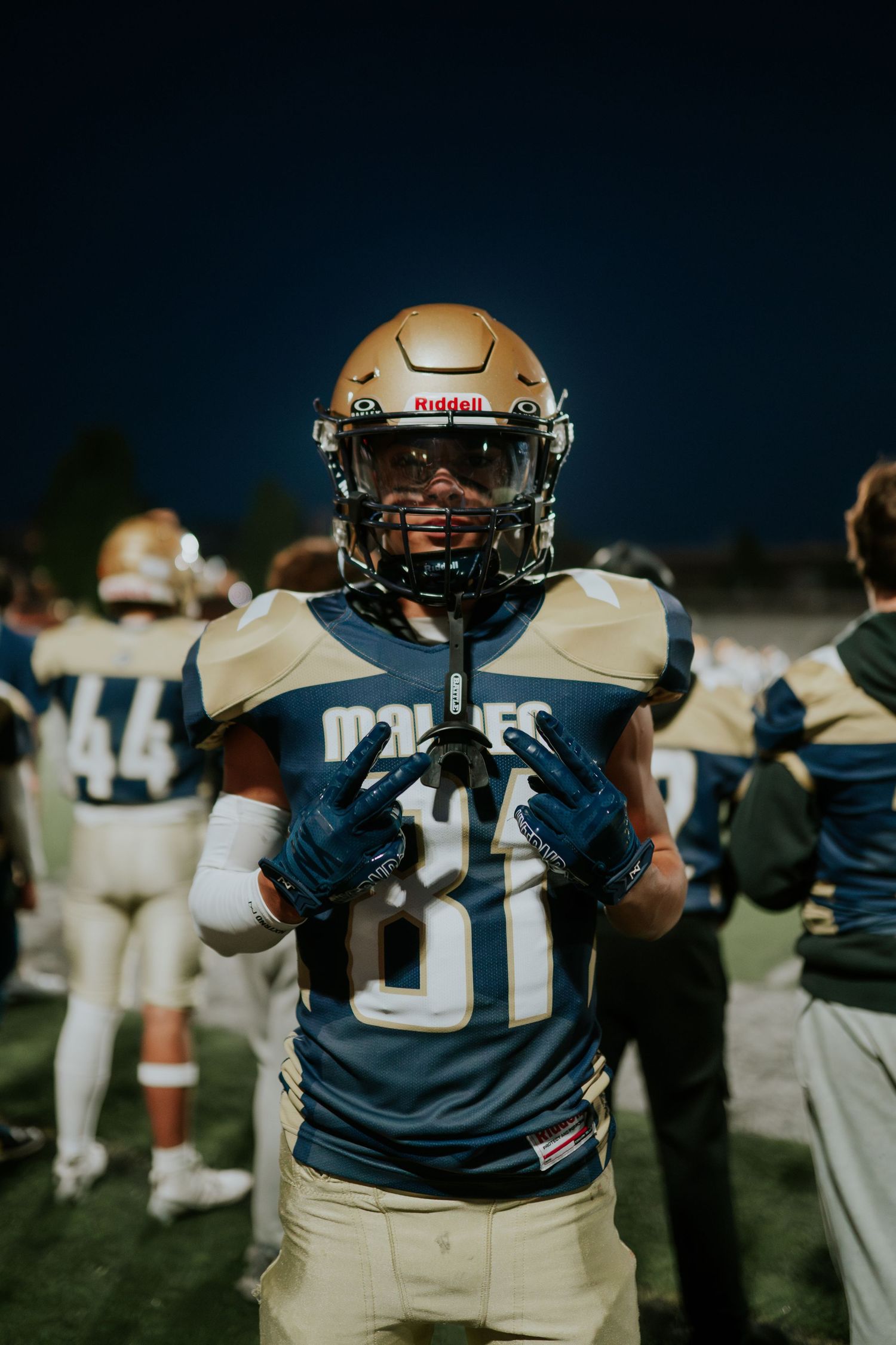 Football player in navy and gold uniform stands on field at night wearing helmet and gloves. Boston MA photographer, Malden MA.