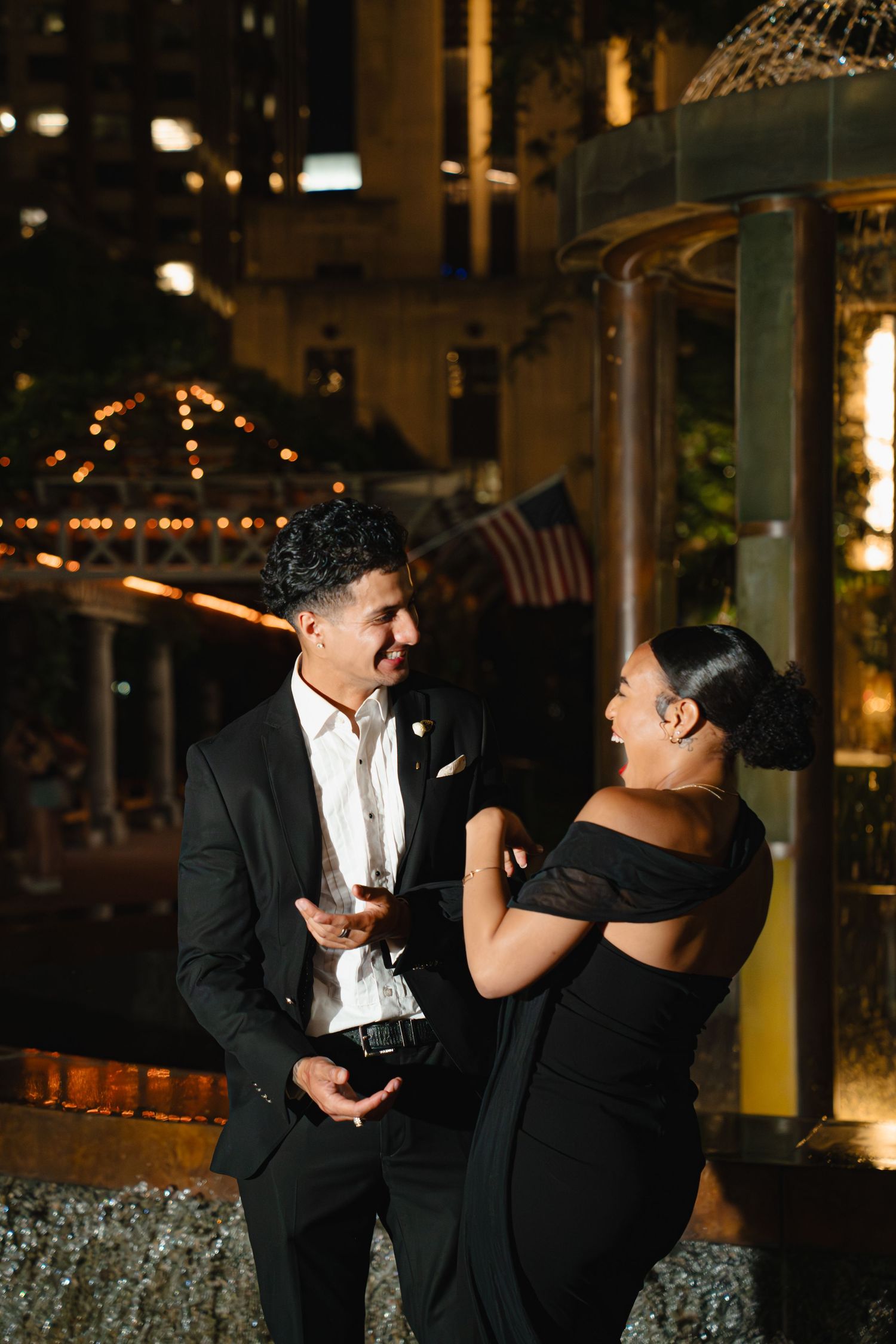 Two people in formal attire share a playful moment during an evening event with twinkling lights in the background. Boston MA photographer.