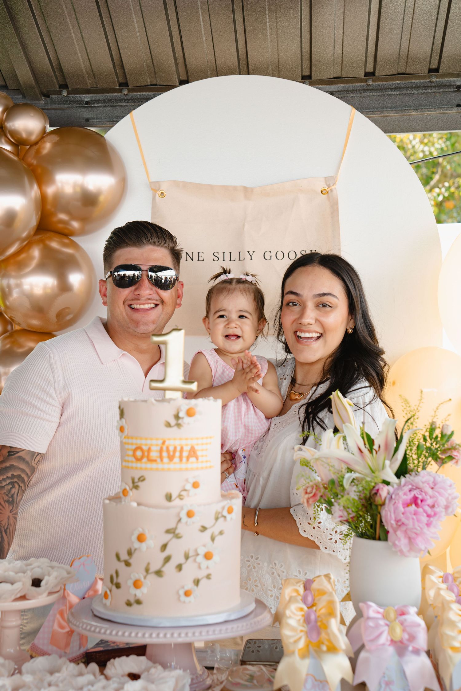 Family gathered around white birthday cake with pink and gold decorations at birthday party. Boston MA photographer, Malden MA.