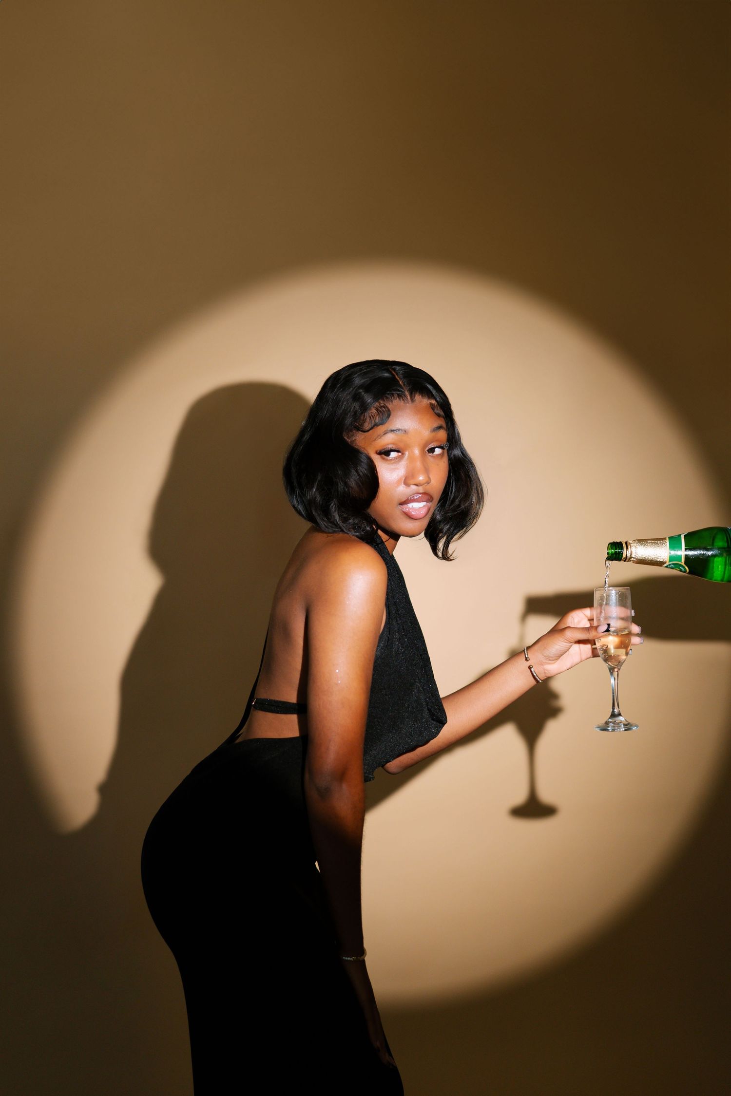 Artistic silhouette photo showing someone in a black dress holding a martini glass against a warm spotlight. Boston MA photographer, Malden.