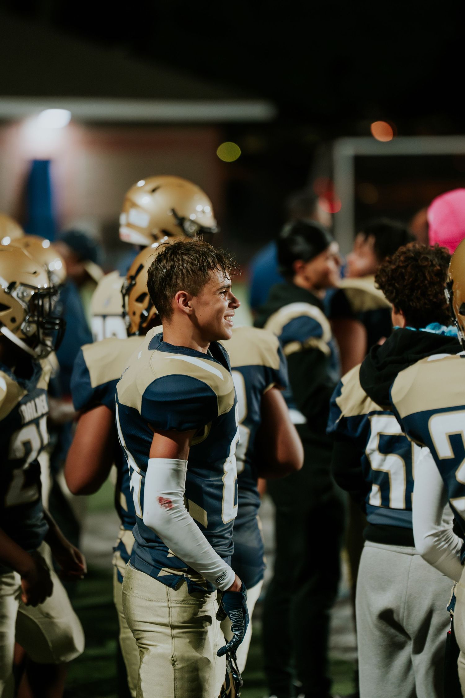 Football players in navy and white uniforms line up on sideline during nighttime game. Boston MA photographer, Malden MA & Greater Boston