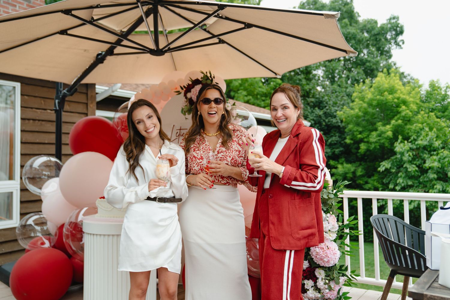 A group gathers on an outdoor patio under beige umbrellas during a birthday celebration. Boston MA photographer, Malden MA.
