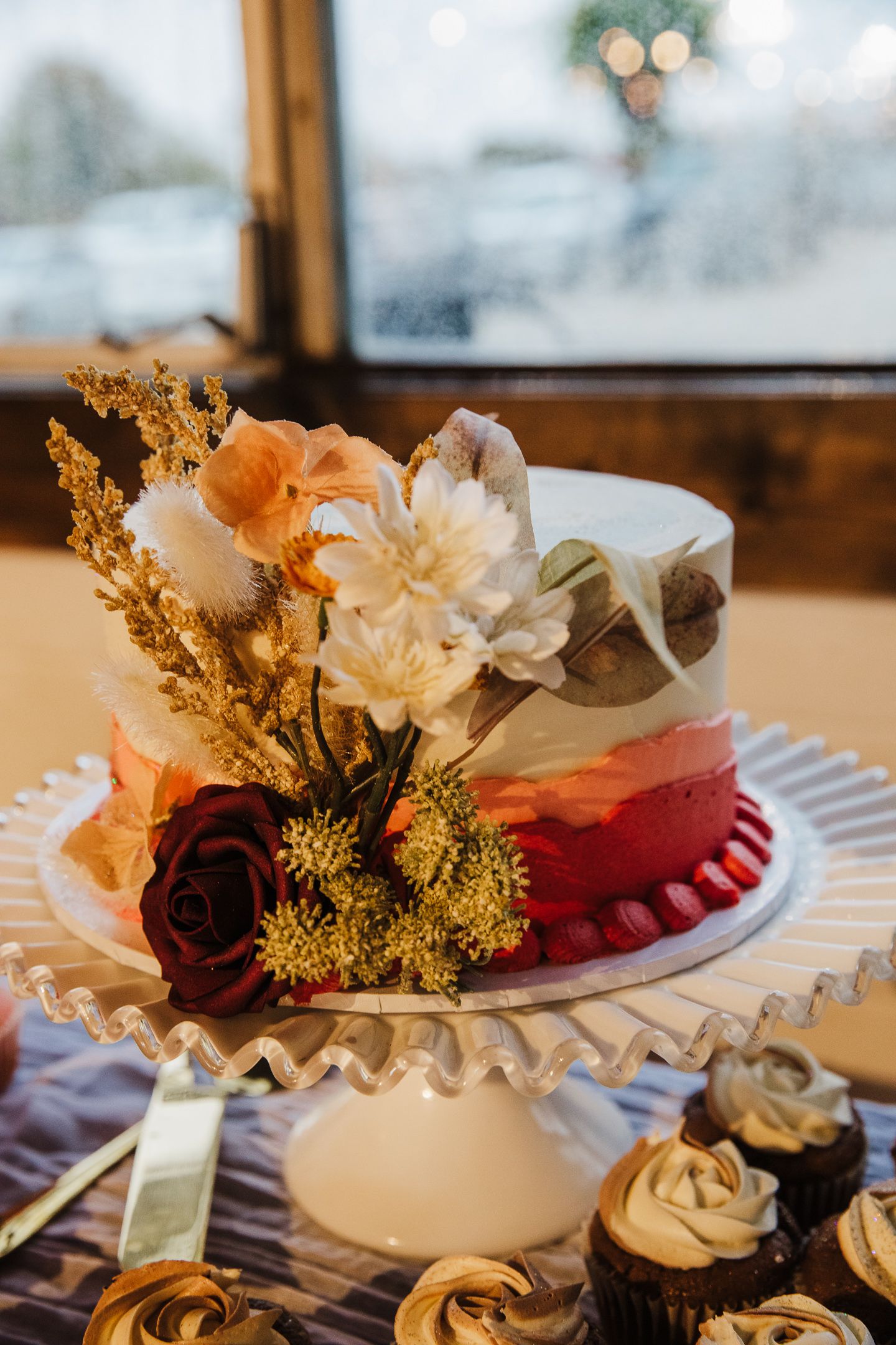 Wedding cake decorated with fresh flowers in peach and burgundy on white cake stand.