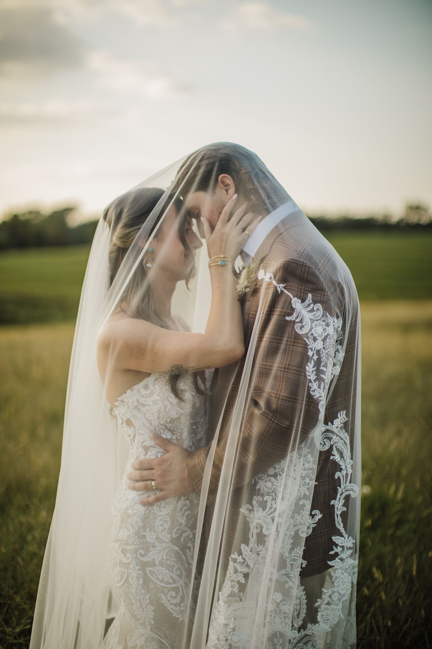 Intimate wedding couple moment captured through an ornate lace veil in a golden field.