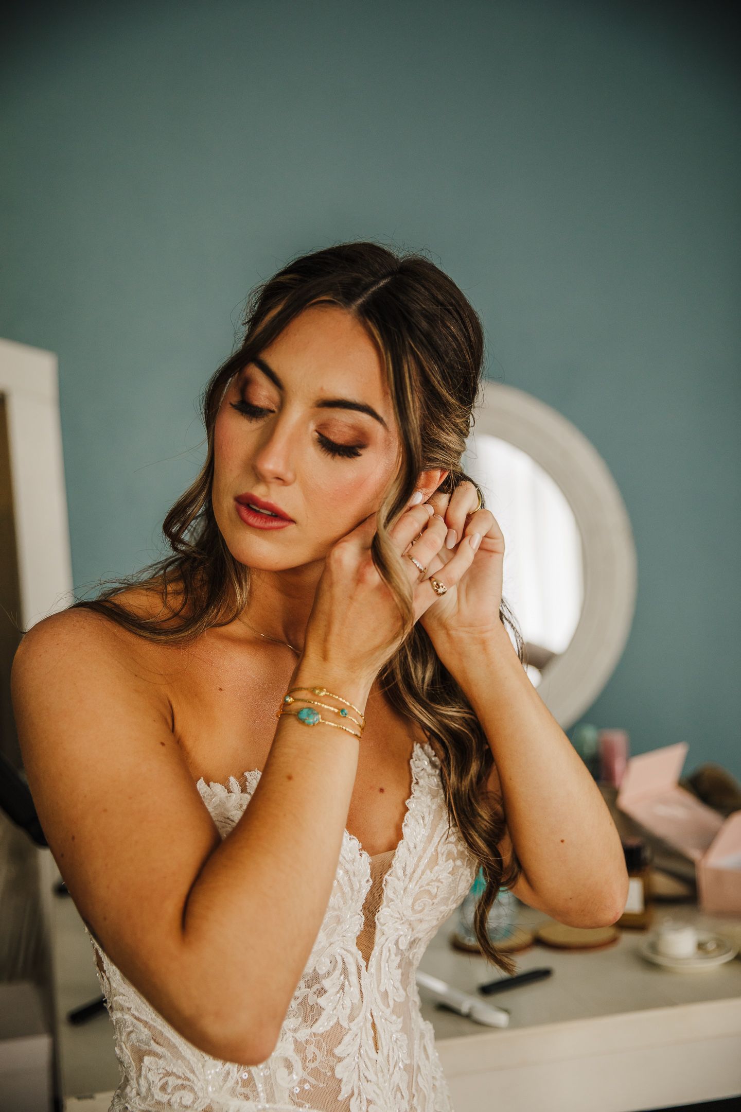 A close-up shot shows elegant bridal jewelry and makeup against a teal background.