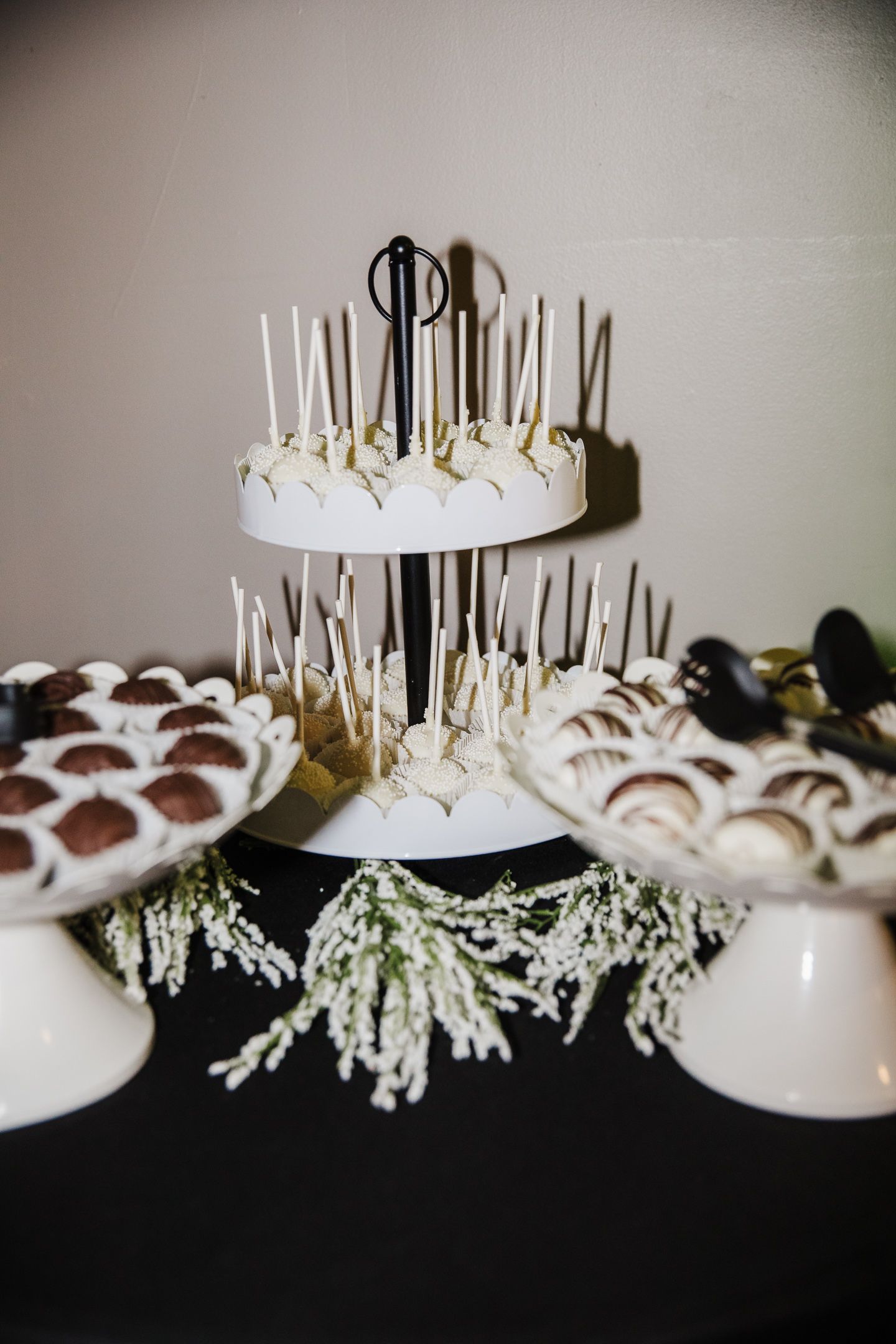 A tiered white wedding dessert display with candles and greenery decorations.