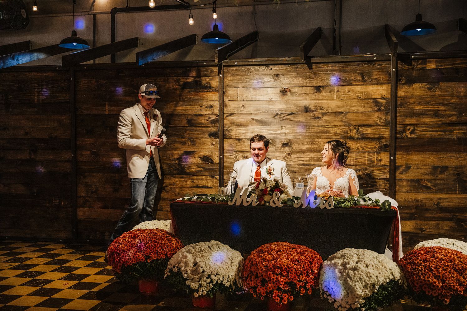 Rustic wedding reception venue with wooden walls, string lights, and red floral arrangements.
