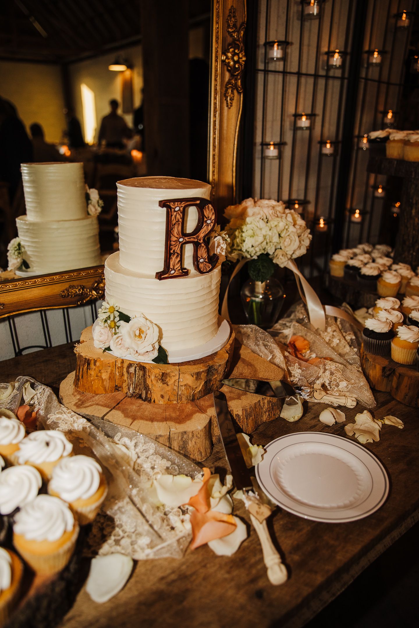 Rustic wedding dessert table with white tiered cake and cupcakes on wood slices.