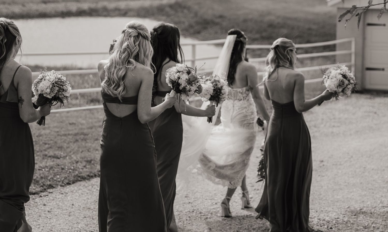 A group of people dance together at an outdoor wedding reception in black and white photography.