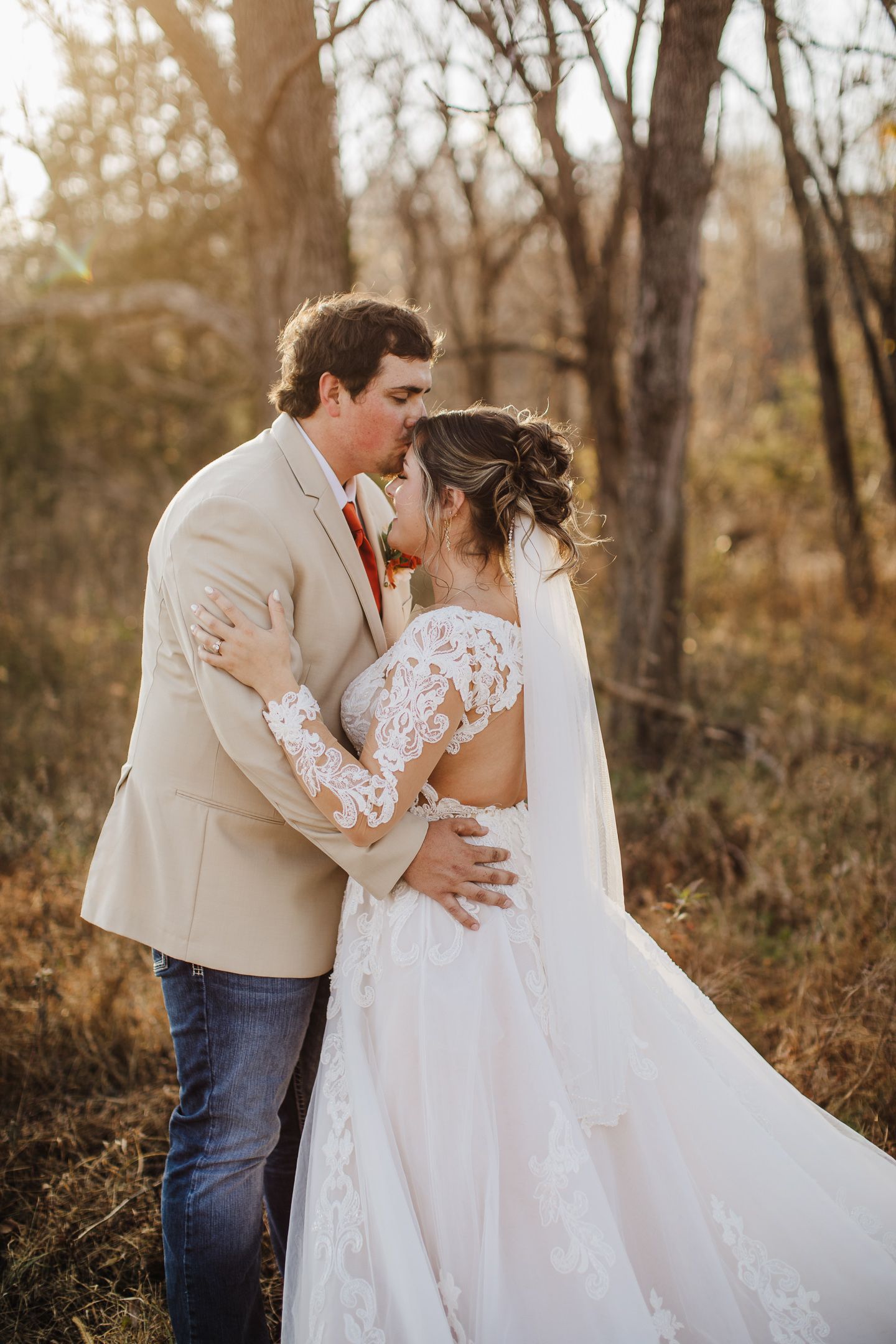 A tender moment between newlyweds in a rustic woodland setting, showcasing a flowing lace wedding dress.