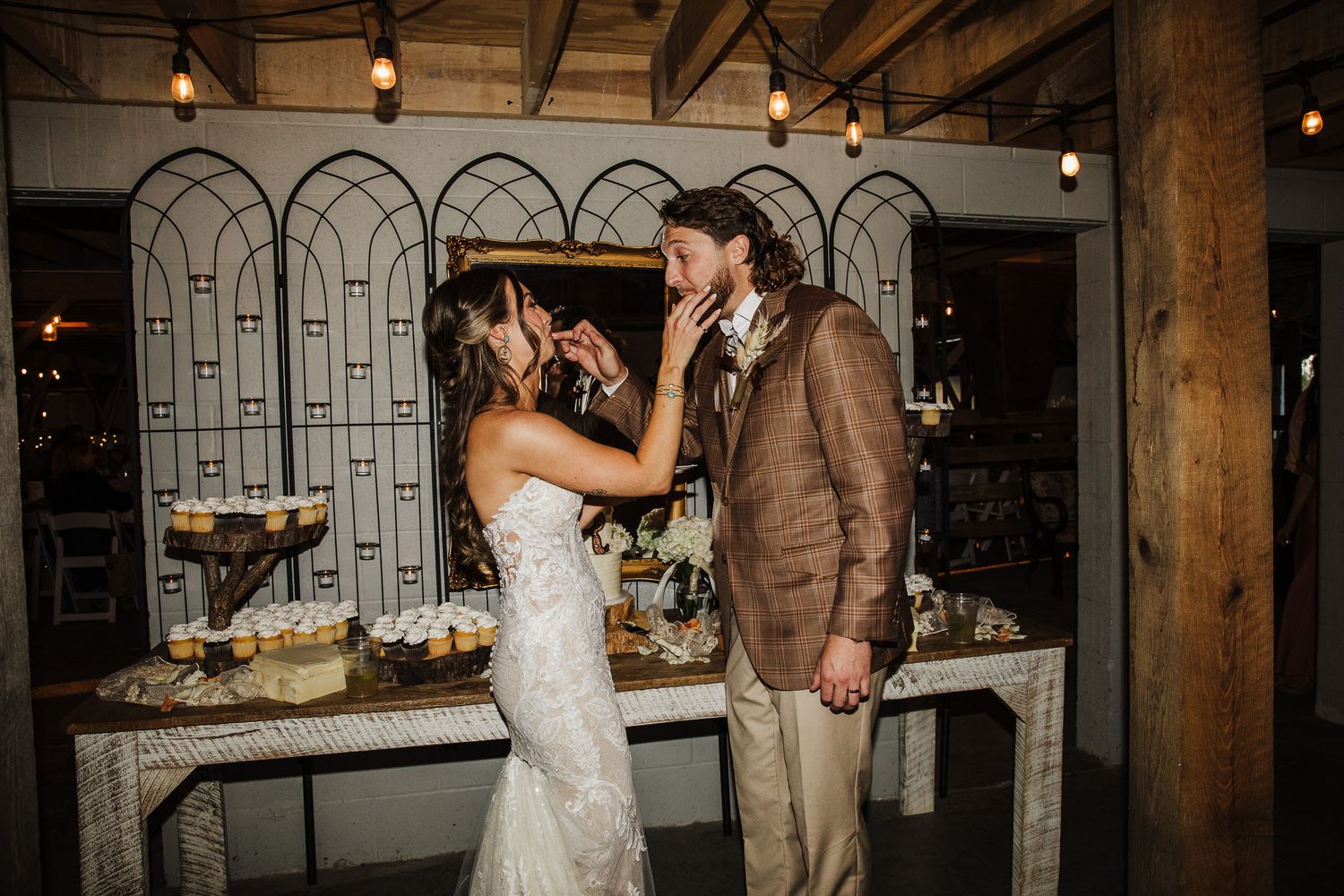 Wedding reception setup in rustic barn venue with exposed beams and string lights.