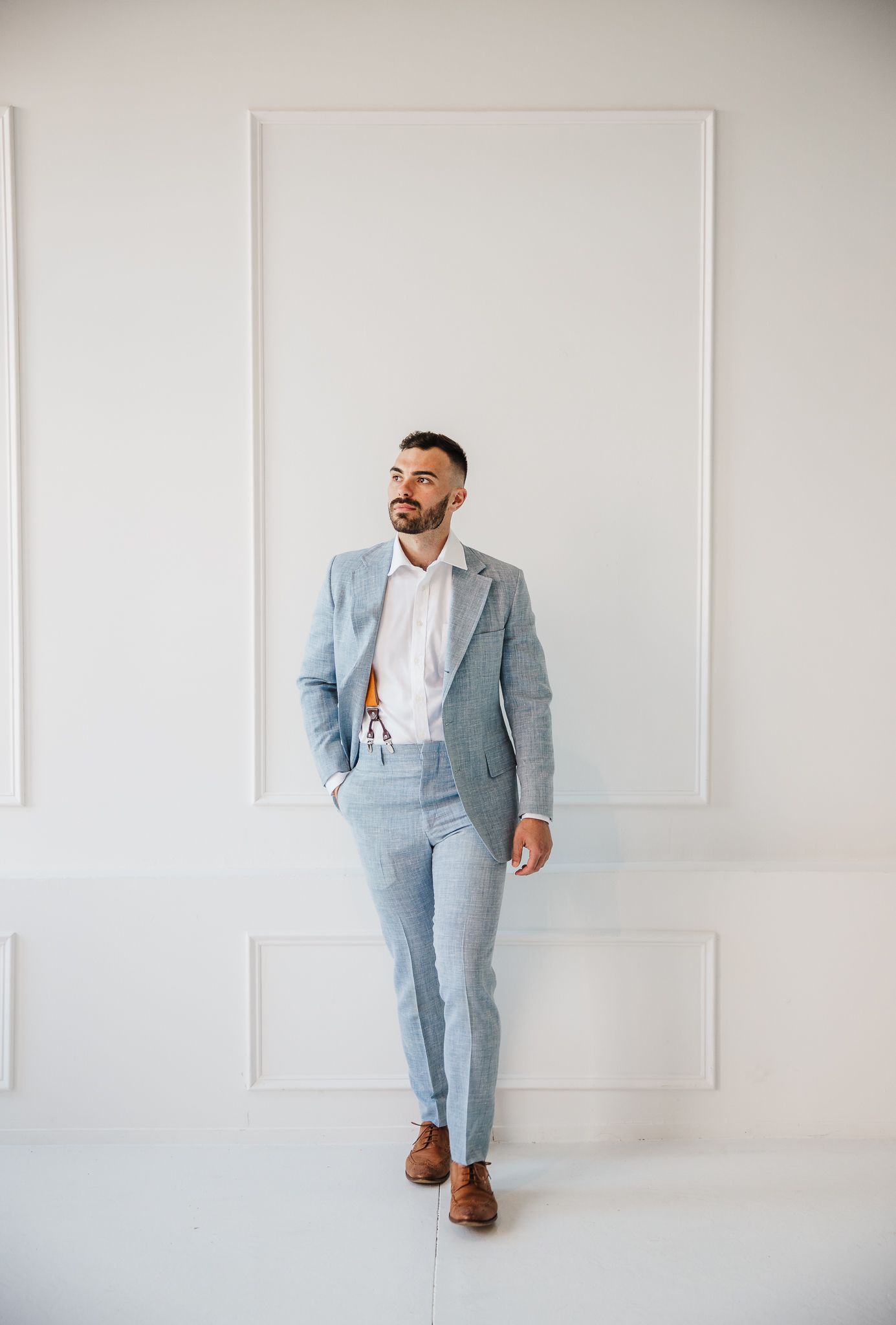 A modern professional in a light blue suit walking against a minimalist white wall background.