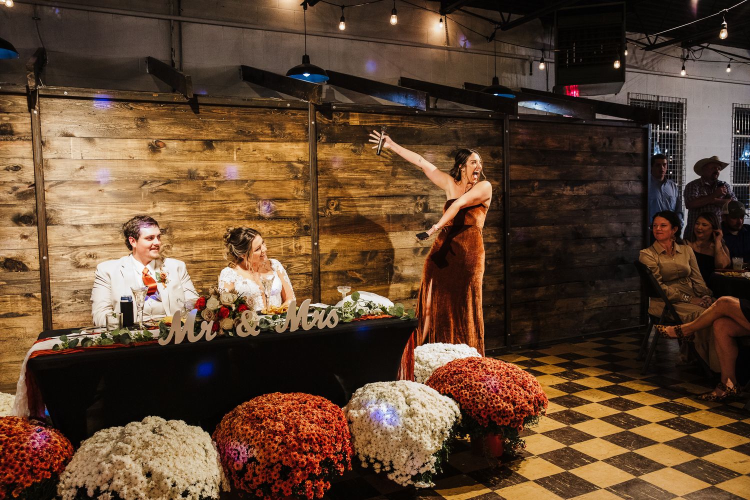 Wedding reception with rustic decor features a black and white checkered floor and warm lighting in an intimate venue.