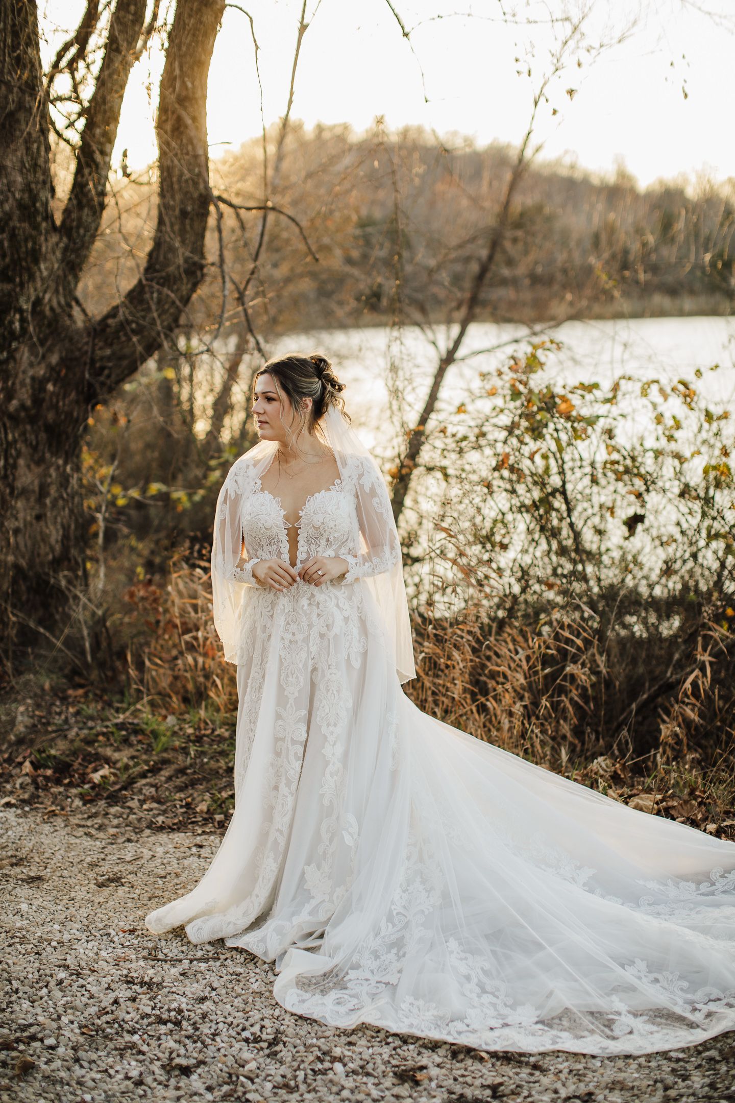 A lace wedding dress with long train photographed by a river during golden hour.