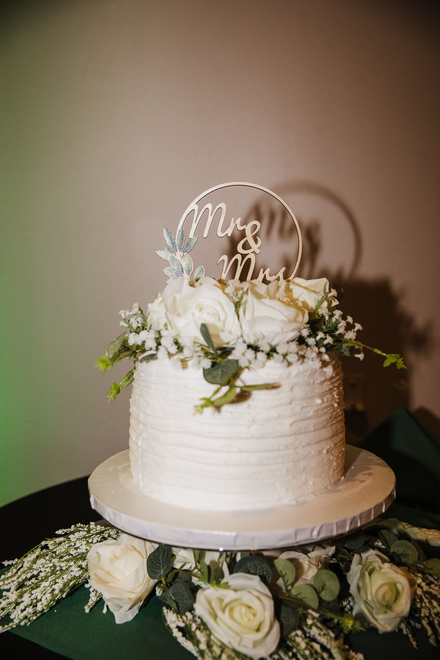 White wedding cake decorated with delicate flowers and a Mr & Mrs topper sits elegantly on display.
