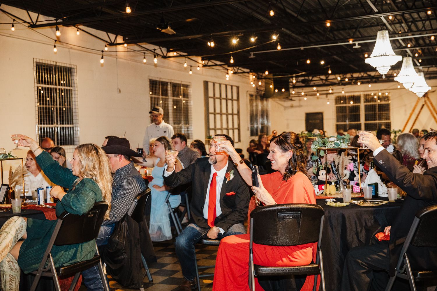 Wedding reception venue with string lights and guests mingling in an industrial space.