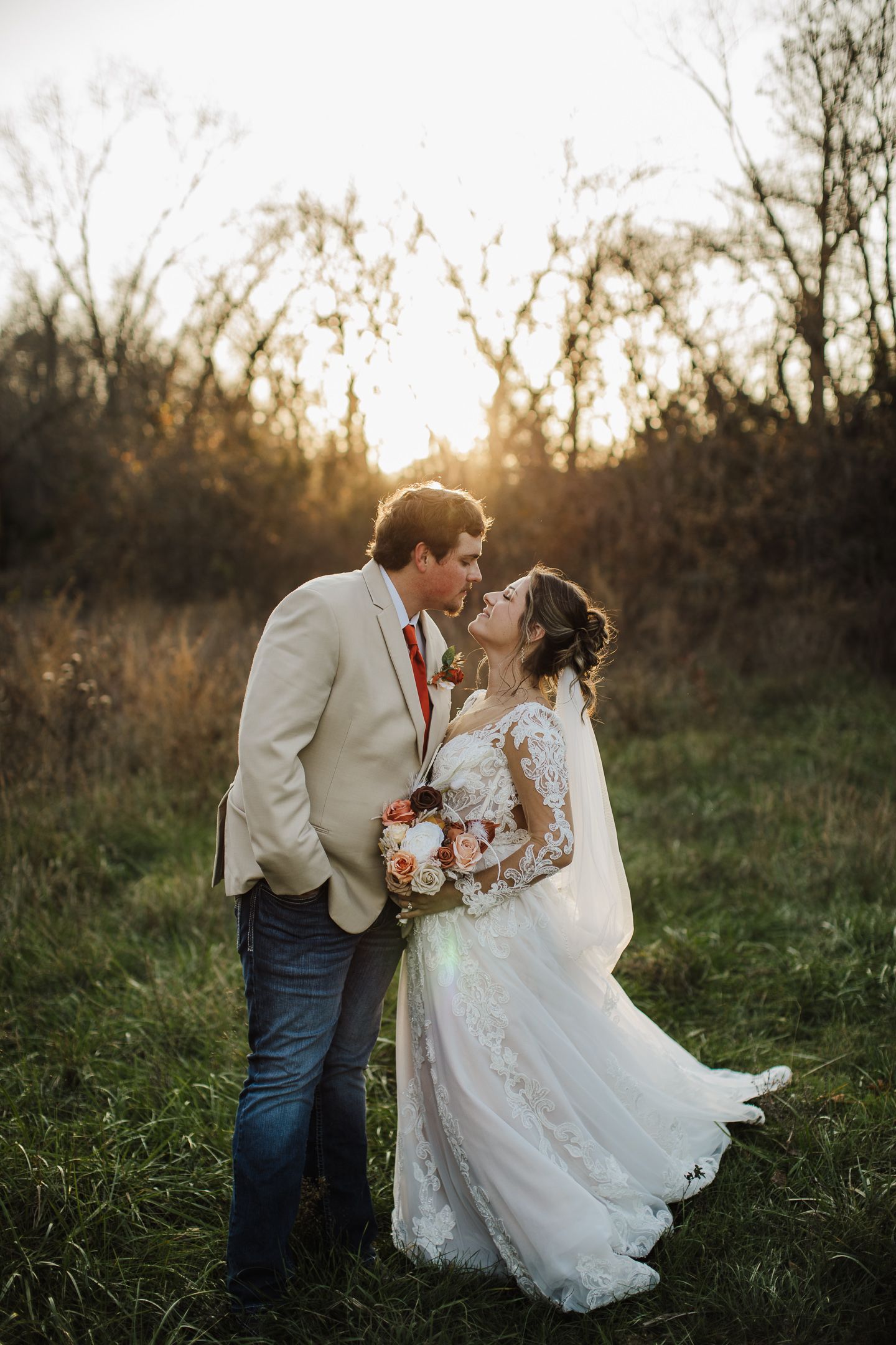 A romantic sunset wedding portrait of a couple in a field with golden light filtering through trees.
