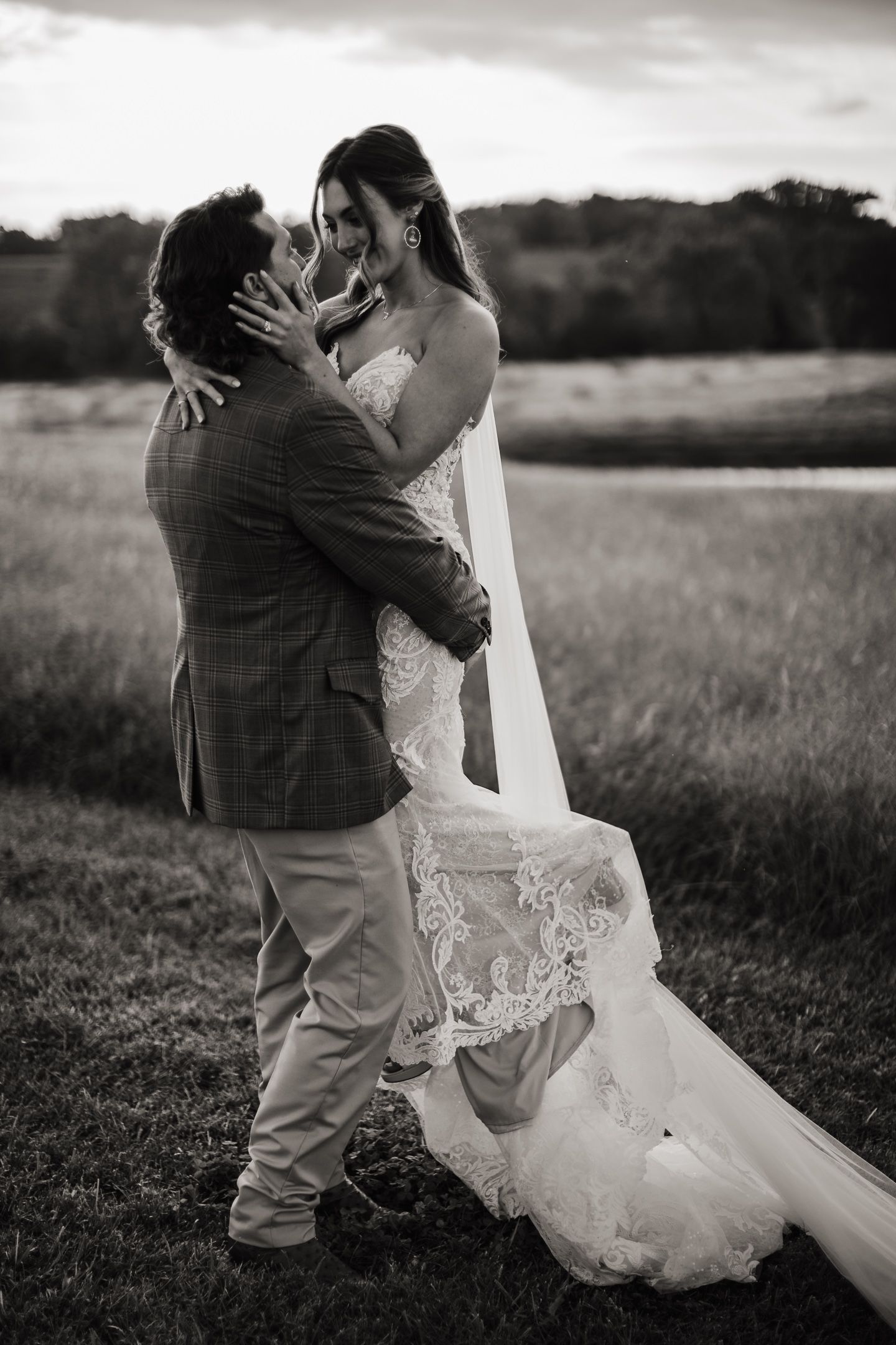 Romantic black and white portrait of a couple embracing in a rustic field.