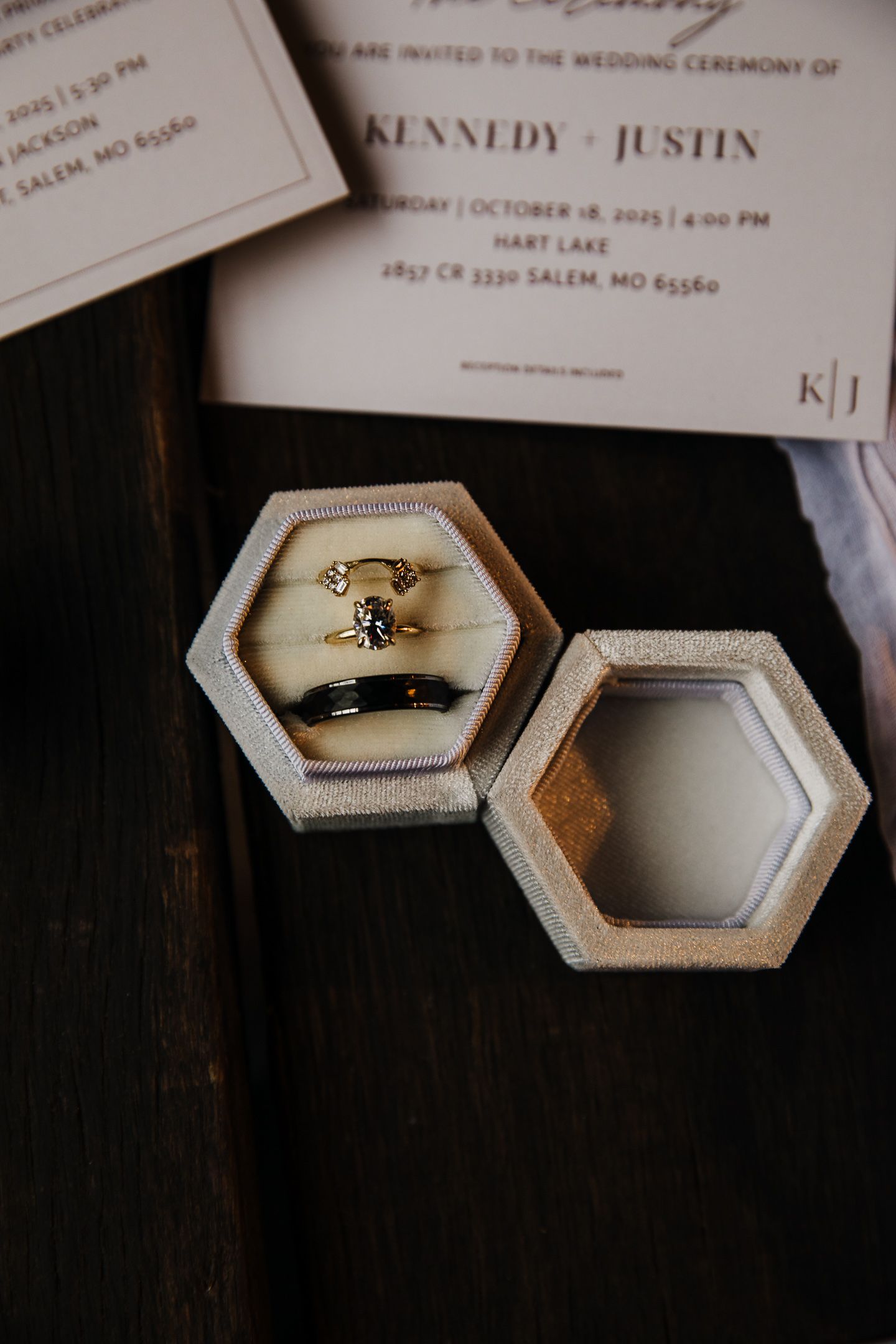 Wedding invitation and rings displayed in hexagonal concrete ring boxes on dark wooden surface.