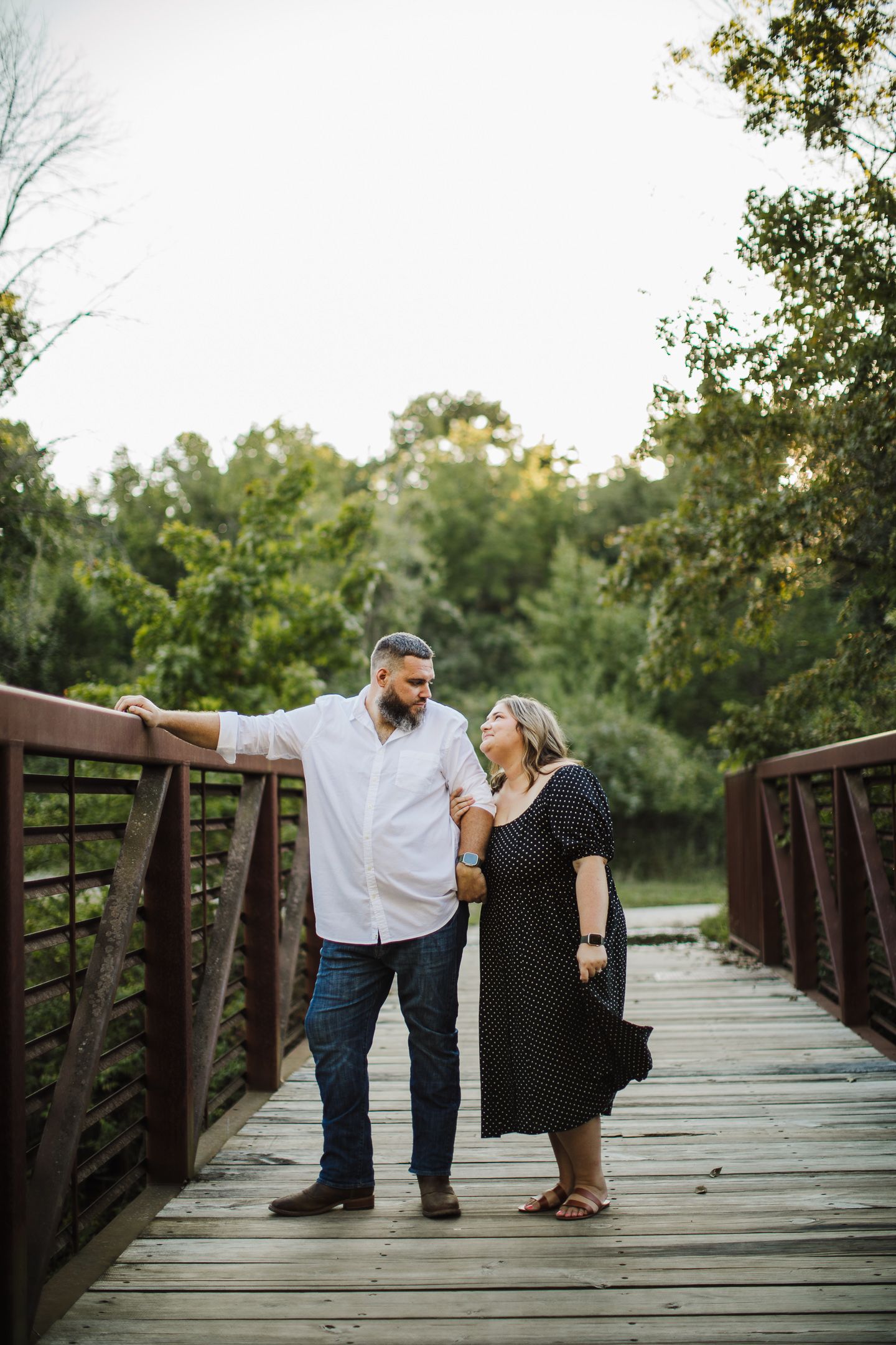 A couple shares playful moments on a wooden bridge in a park setting.