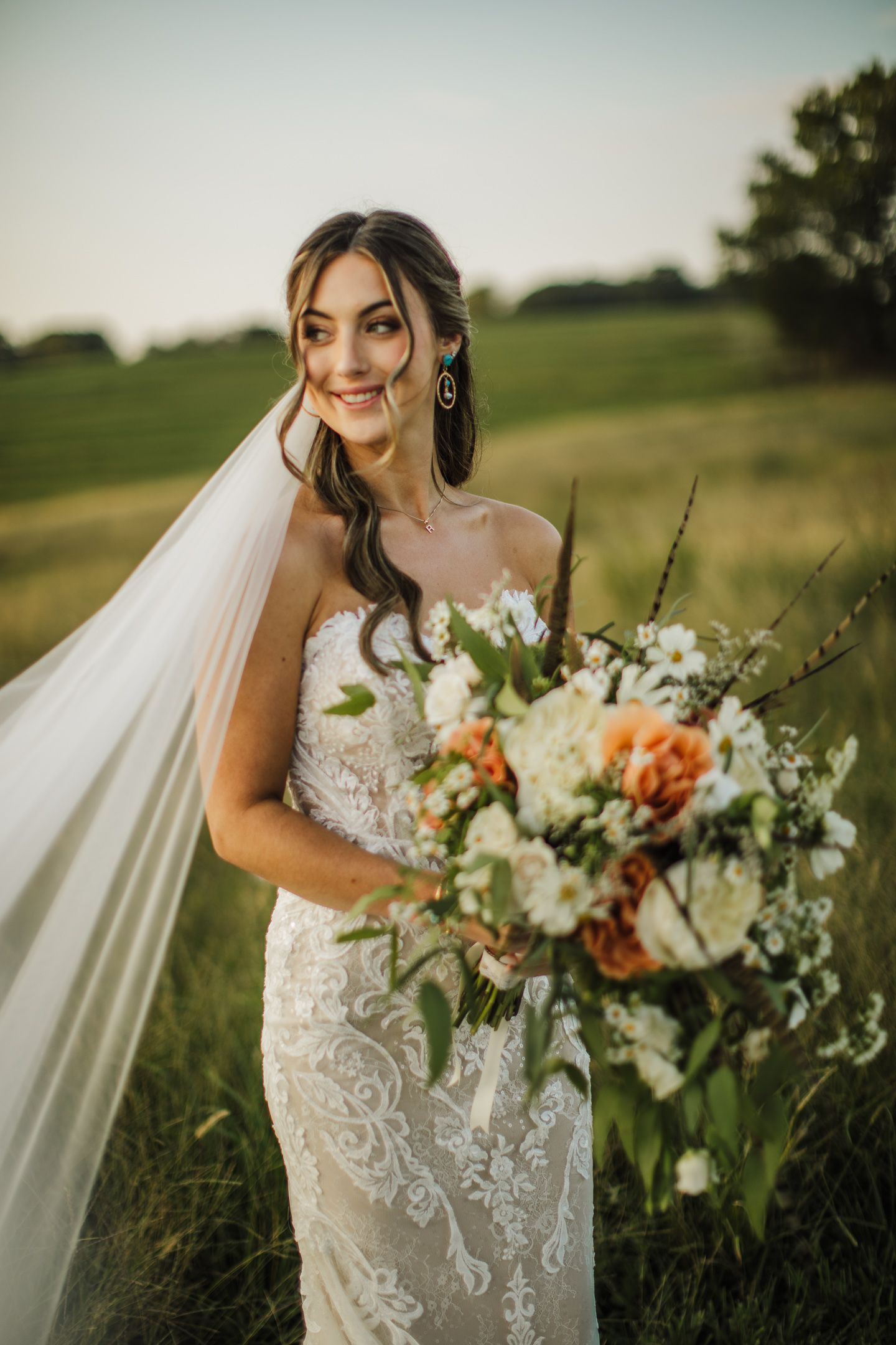 Beautiful lace wedding dress and bouquet photographed in a golden field at sunset.