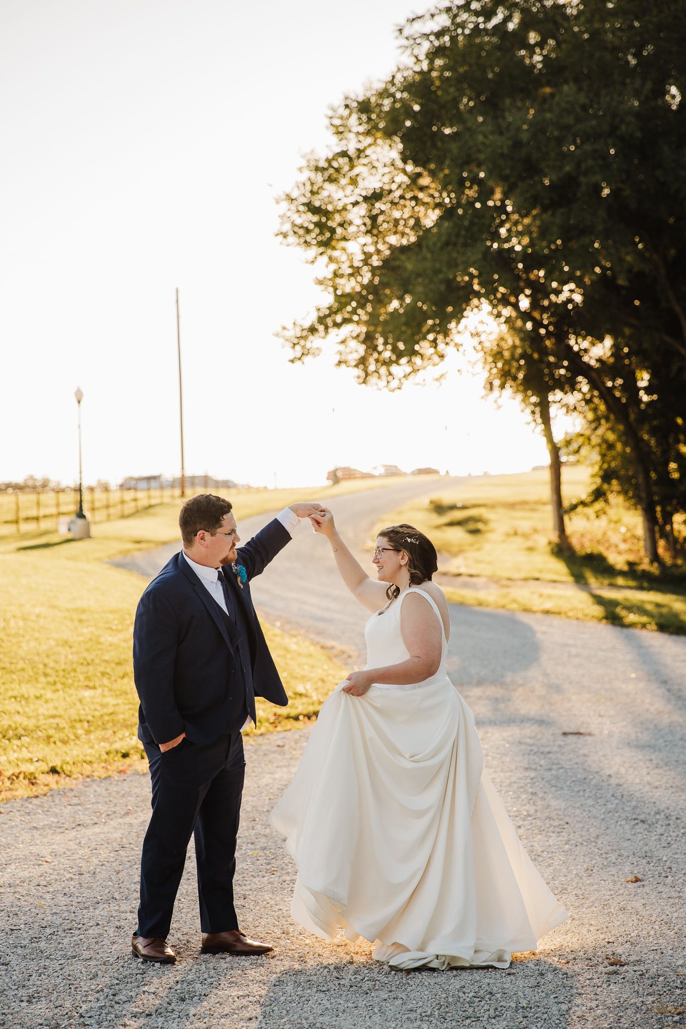 Playful wedding couple dancing and twirling on a sunlit country road.