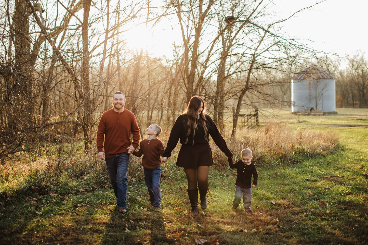 A family walks together holding hands on an autumn path through the woods.