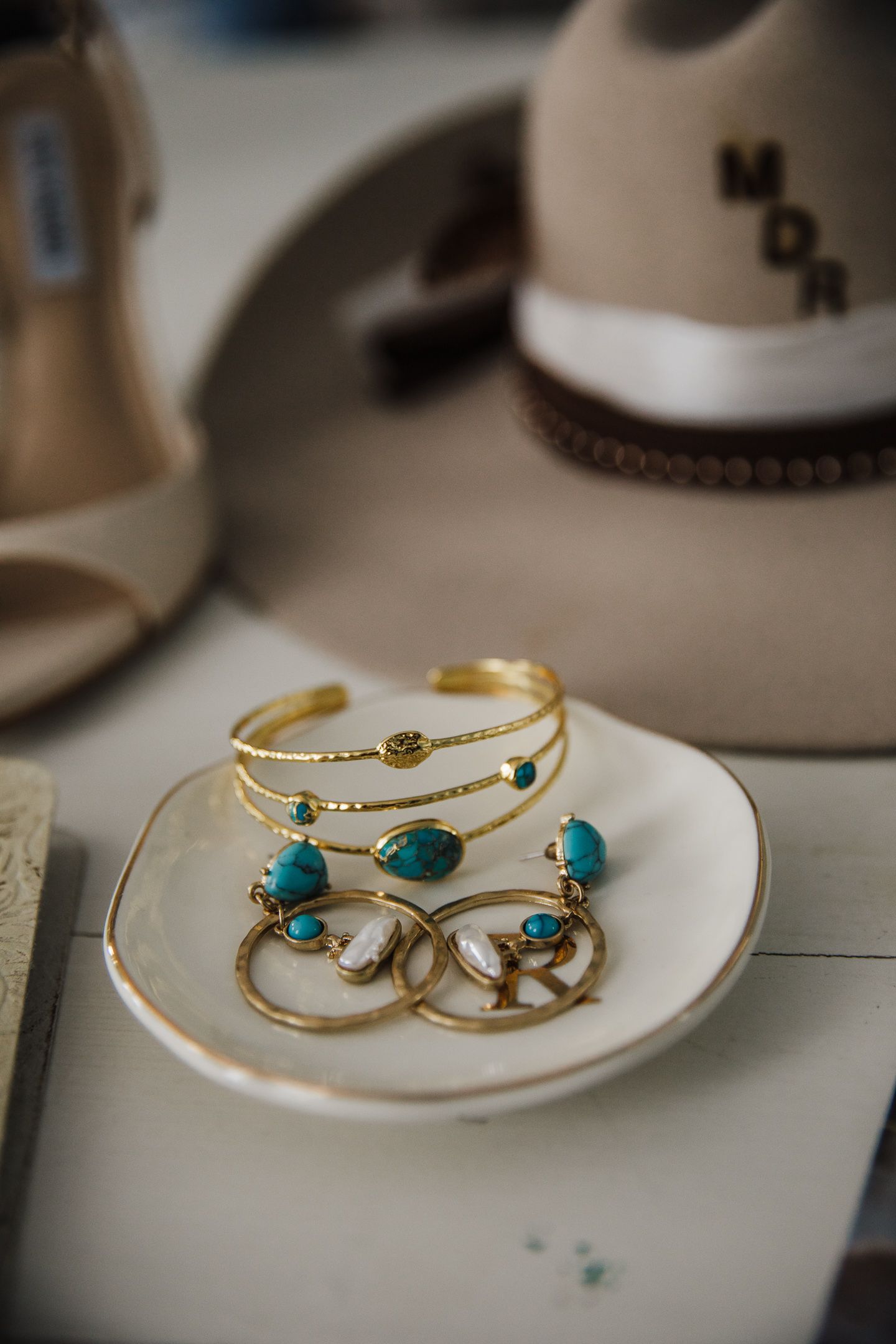 Turquoise and gold jewelry set displayed on small white plate with wedding accessories.