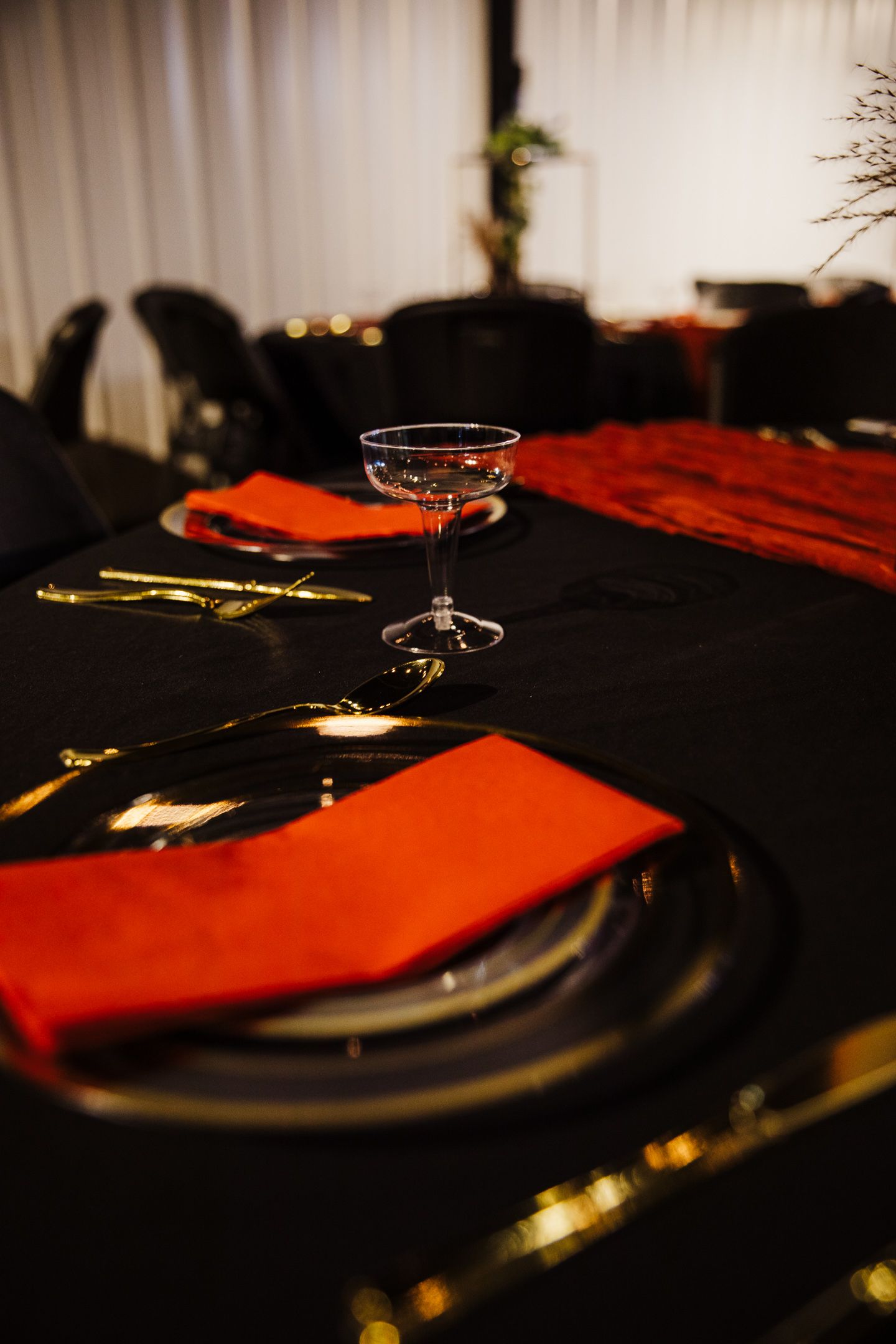 Moody table setting with black linens, orange napkins, and vintage champagne glass.