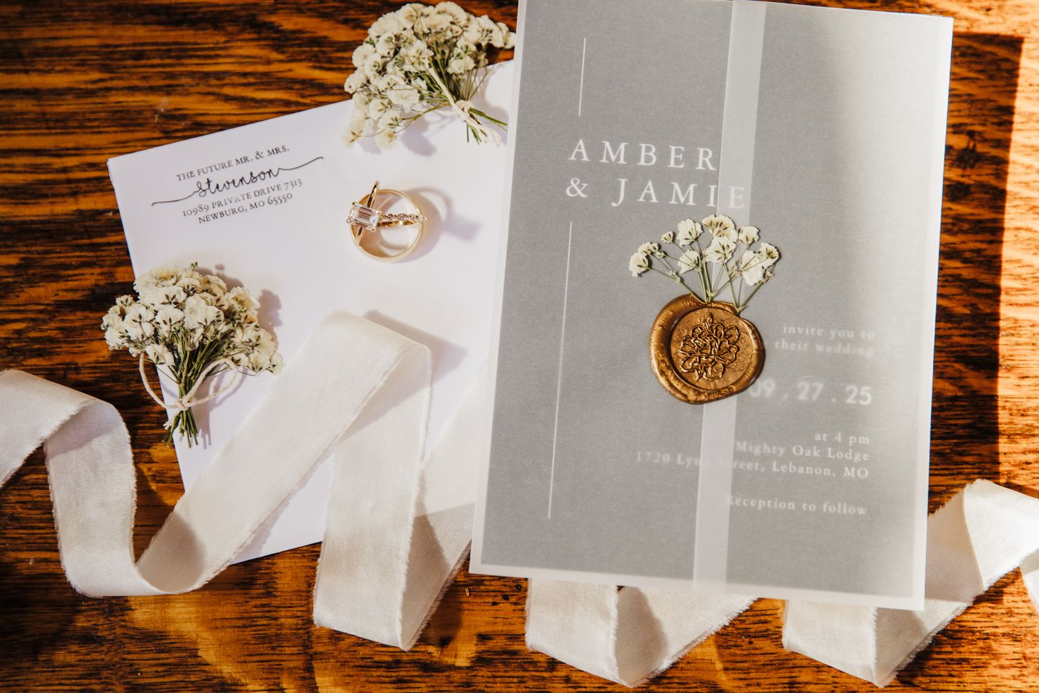 Elegant wedding invitation with wax seal and white flowers on wooden surface.